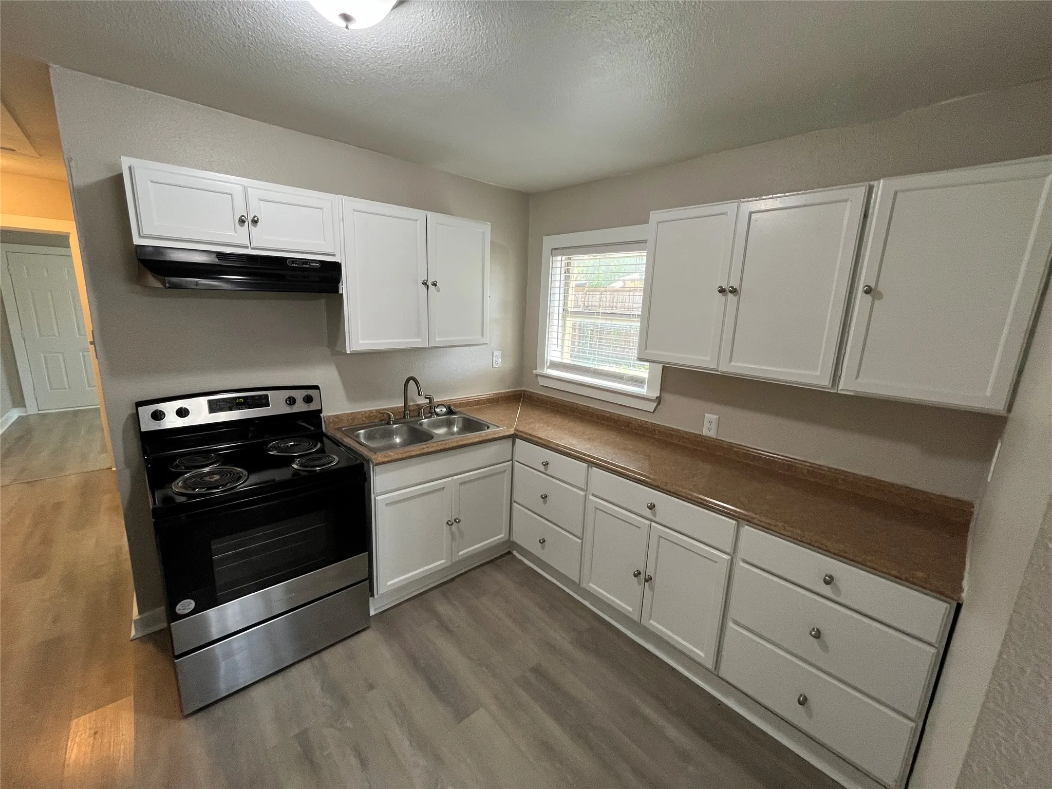 Kitchen featuring white cabinetry, stainless steel range, and wood-finish flooring