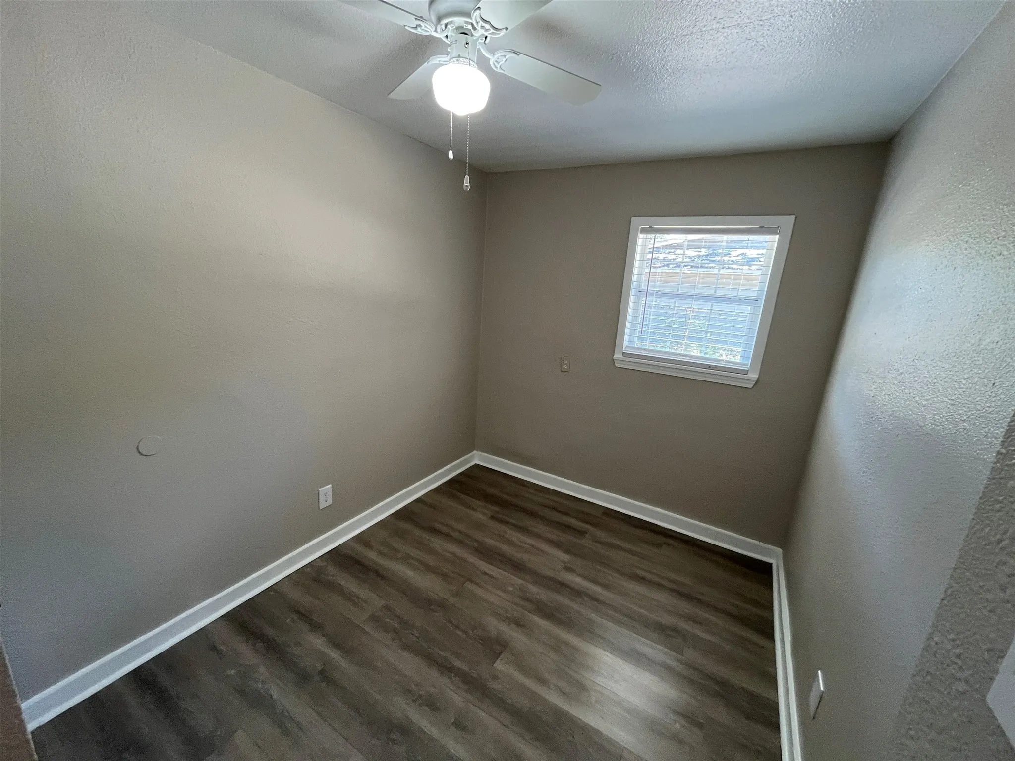 Room featuring wood-finish flooring, a window with blinds, a white ceiling fan with integrated lighting, and neutral-toned walls with white baseboards