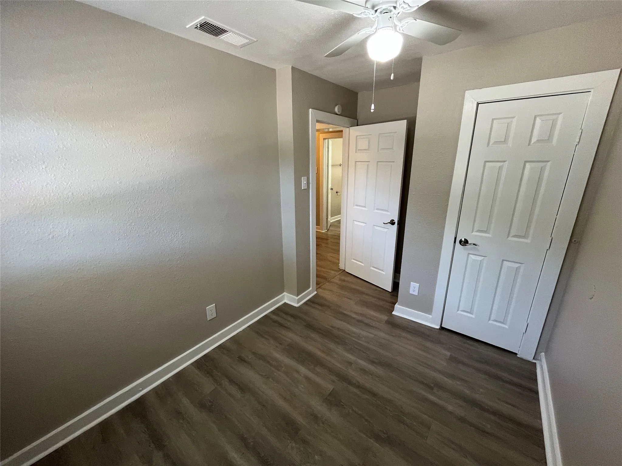 Spacious room featuring wood-finish flooring, neutral-toned walls, a ceiling fan, and white trim molding