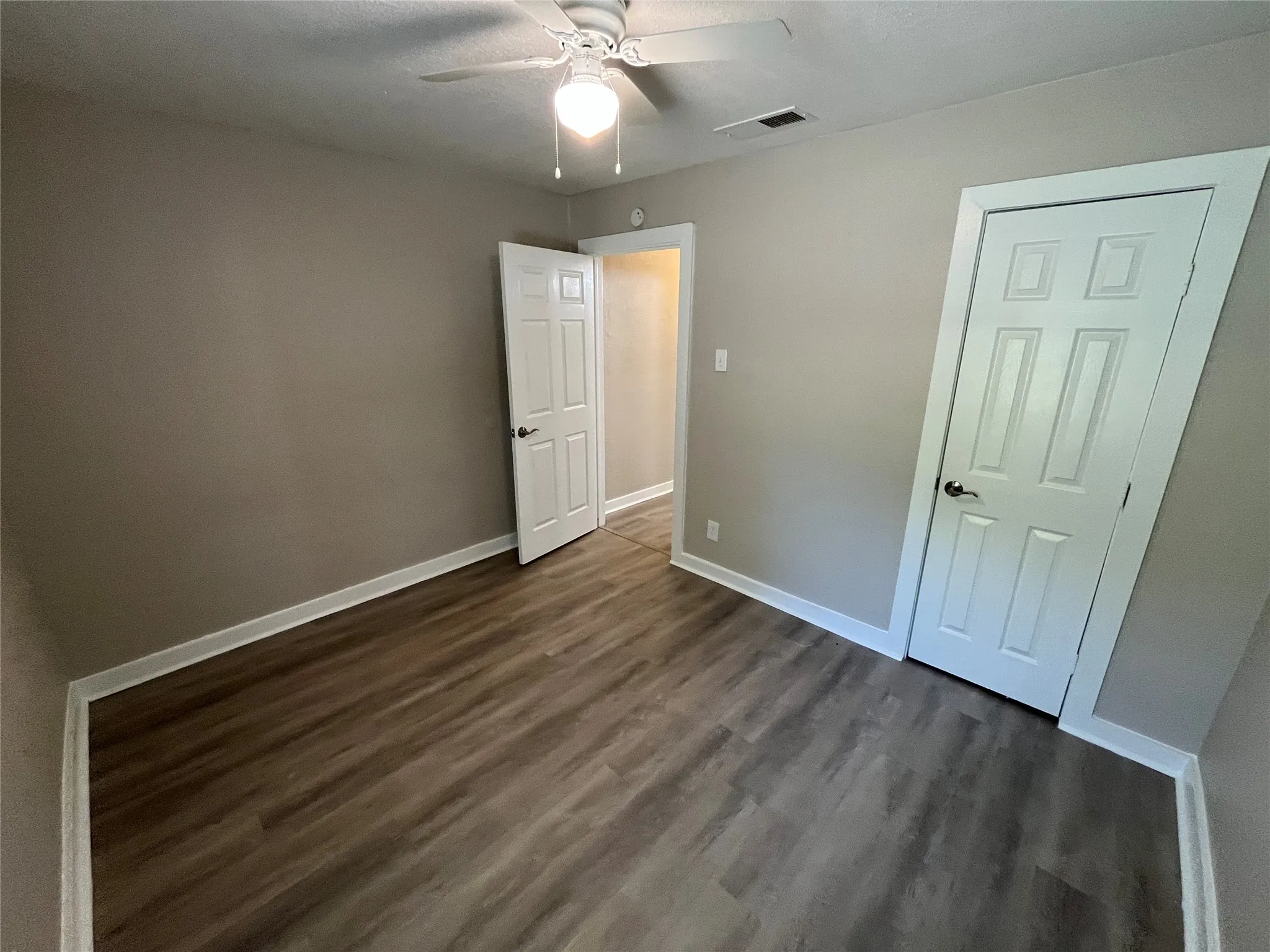 Room featuring wood-finish flooring, neutral wall tones, white trim, a ceiling fan with light fixture, and paneled doors