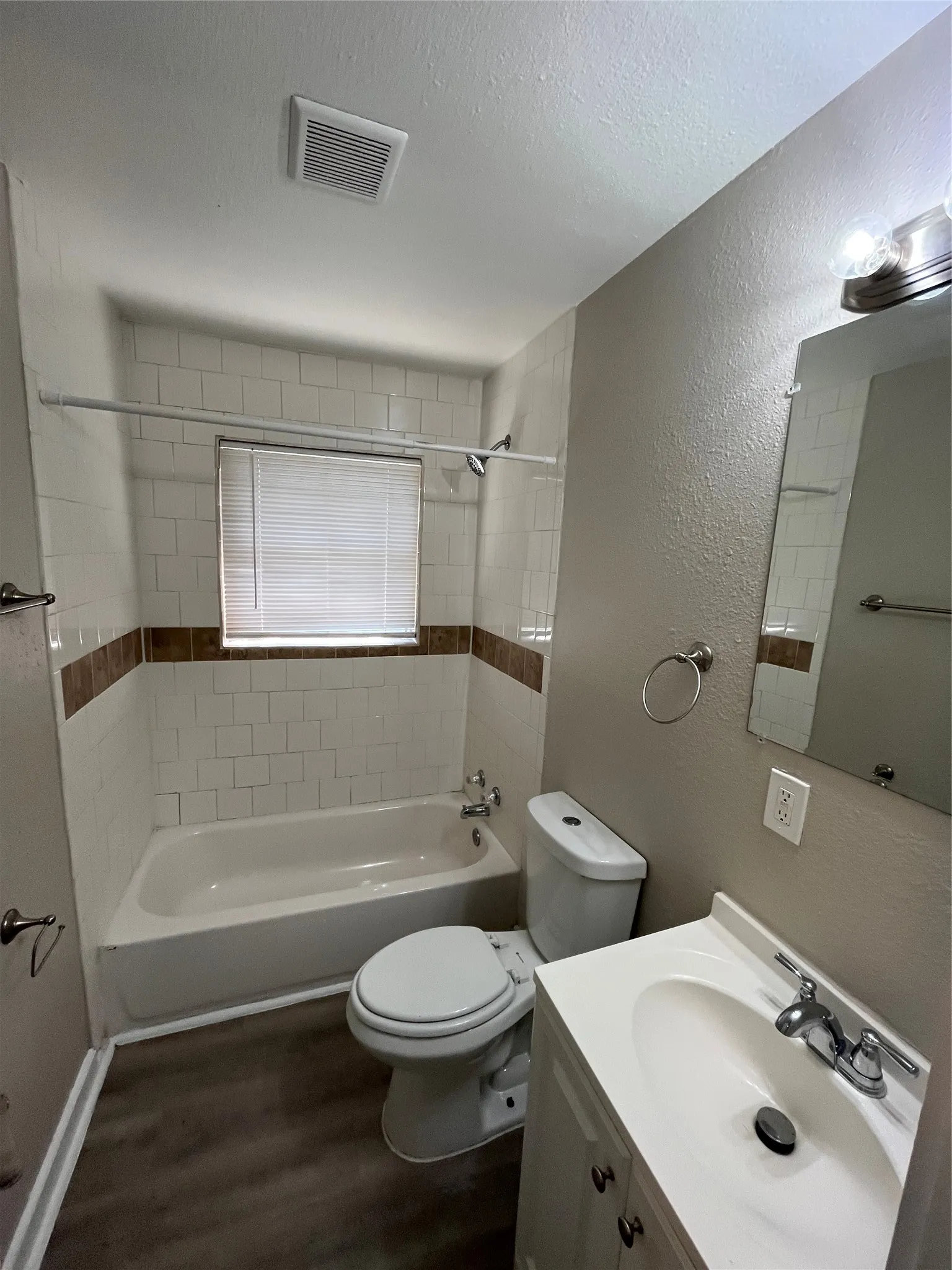 Full bathroom featuring a white bathtub, ceramic tile surround with decorative accent, a toilet, and a vanity with an integrated sink