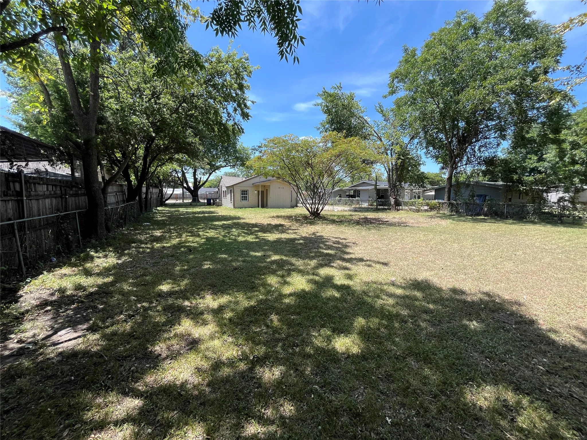 Expansive backyard featuring mature trees, a manicured lawn, and a partial chain-link fence