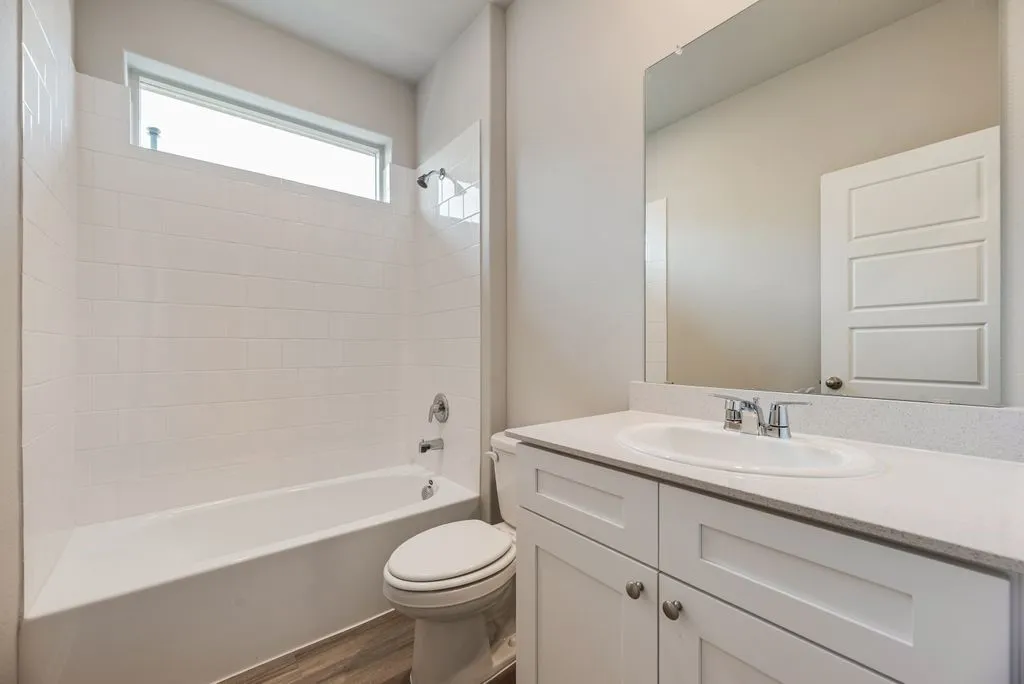 Full bathroom featuring a white tub with subway tile surround, an overhead window, and a vanity with a white countertop and integrated sink