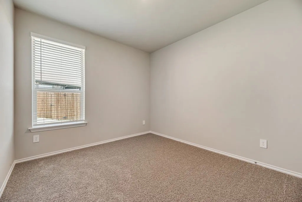Bedroom featuring neutral-toned walls, plush carpet flooring, a single window with blinds, and white trim