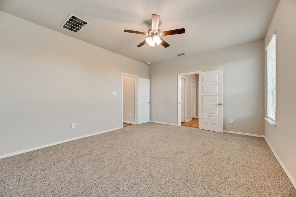Spacious room featuring neutral carpeting, light gray walls, a ceiling fan with integrated lighting, and white paneled doors