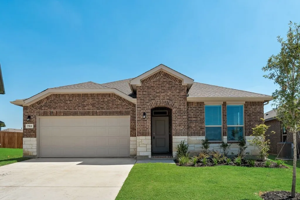 Brick and stone facade residence featuring an attached two-car garage, mature landscaping, a concrete driveway, and covered entry