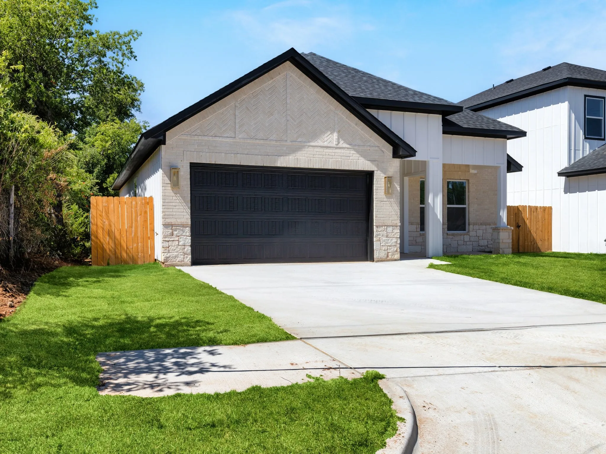 Contemporary residence featuring a two-car garage, light-colored brick and stone exterior, a dark shingle roof, and a concrete driveway