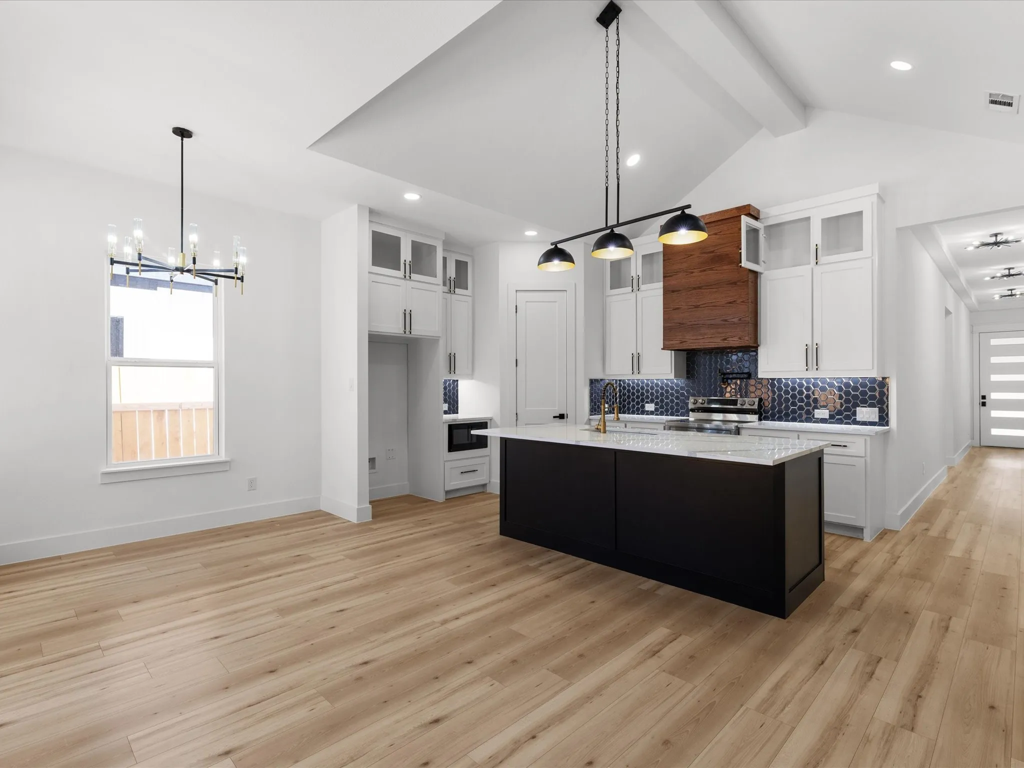 Spacious kitchen featuring a large island with a light-colored countertop, white cabinetry with clear glass accents, and a dark honeycomb tile backsplash