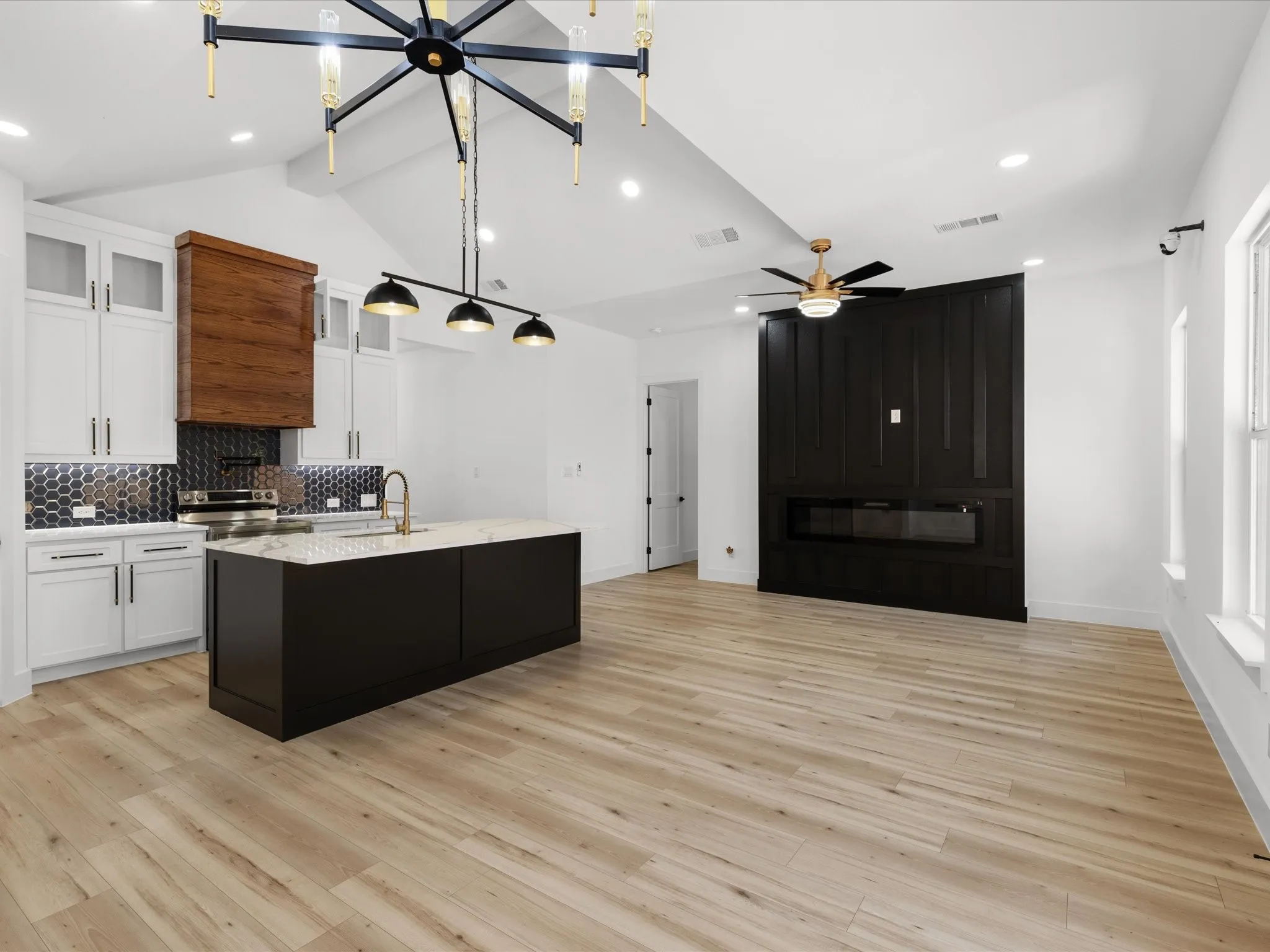 Open-concept interior featuring light wood-finish flooring, a contemporary kitchen island with a light-colored countertop, and a built-in linear fireplace with a dark paneled surround