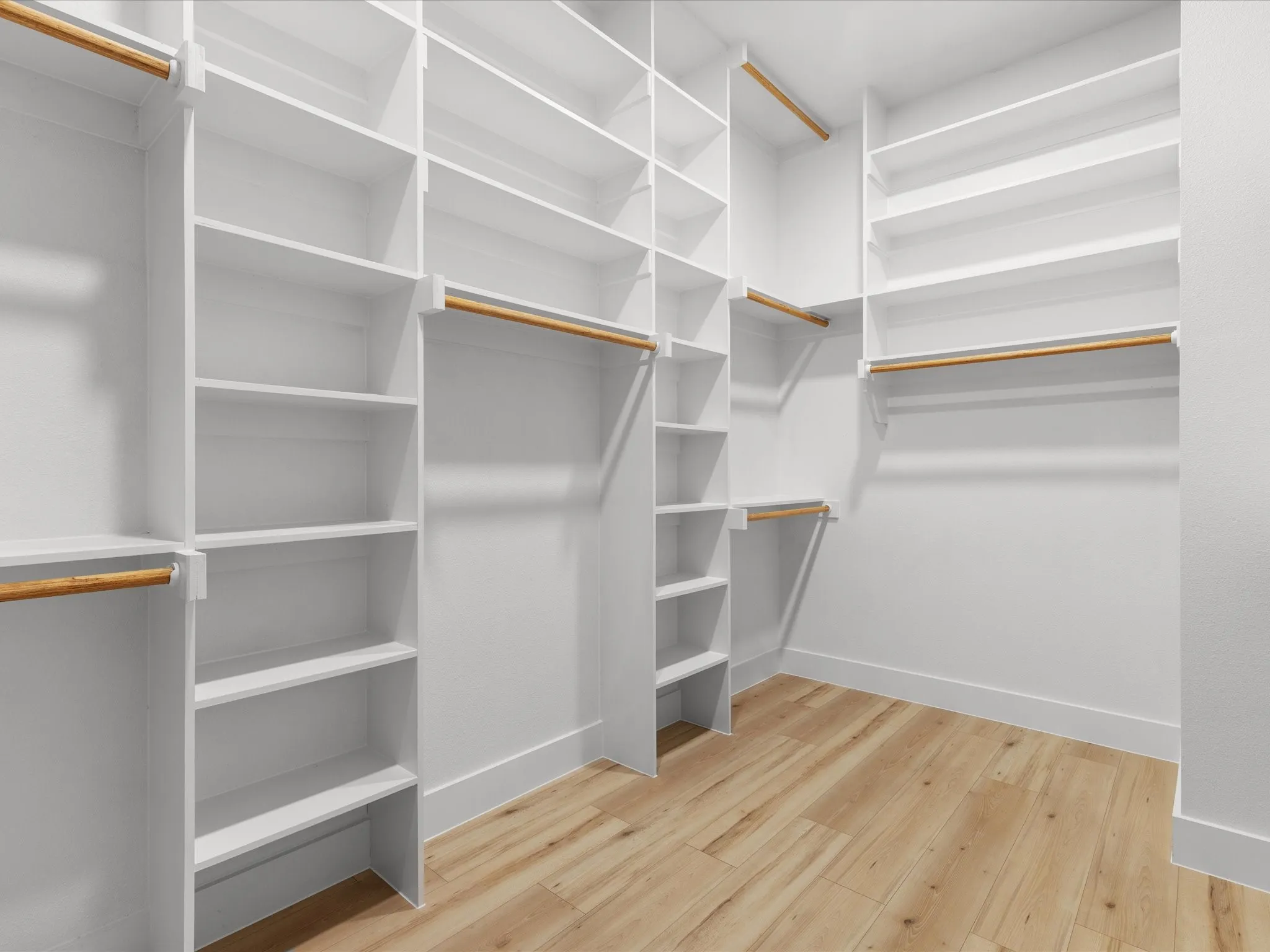 Spacious walk-in closet featuring extensive built-in shelving, multiple hanging rods, and wood-finish flooring