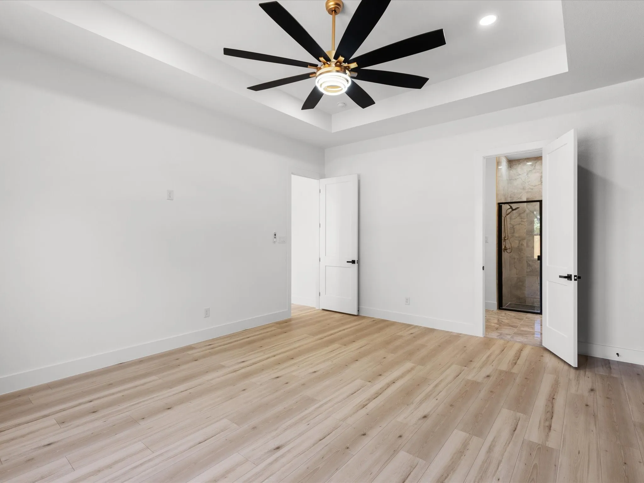 Spacious room featuring wood-finish flooring, a tray ceiling with a modern ceiling fan, and white walls