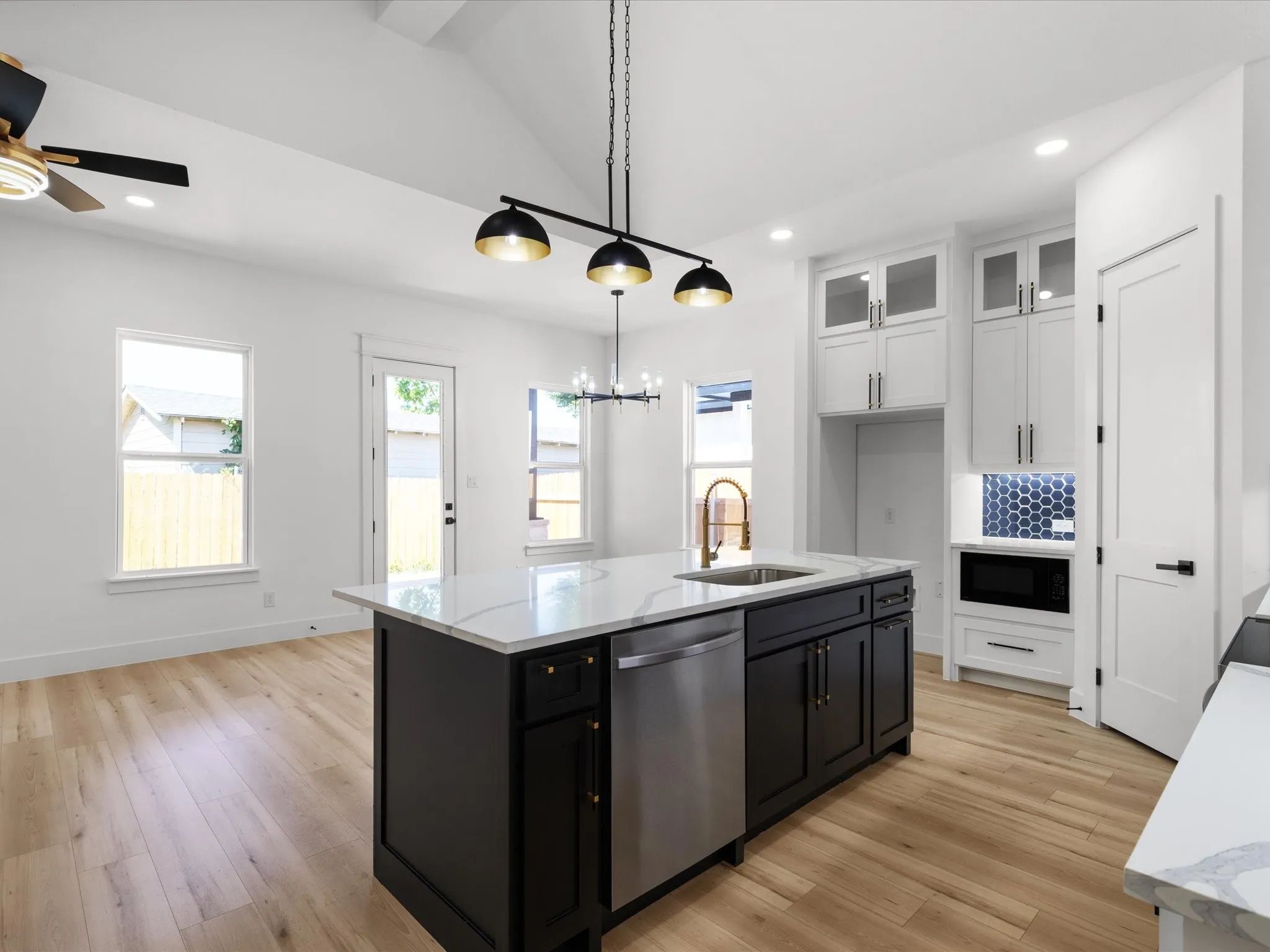 Contemporary kitchen featuring a large island with a white countertop and dark cabinetry, stainless steel dishwasher, and a bronze-finish faucet
