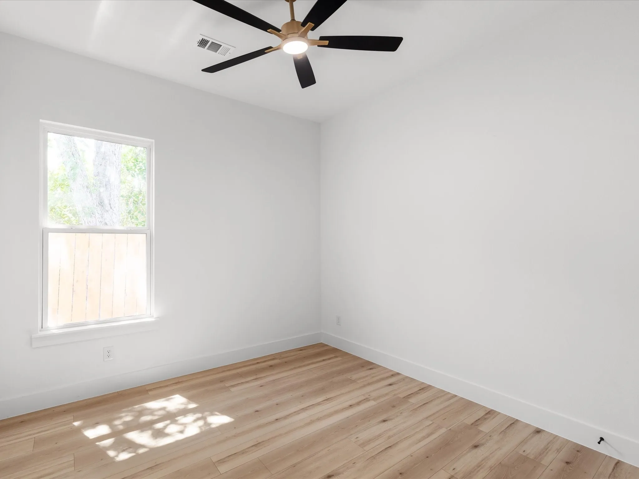 Bright interior space featuring light wood-finish flooring, a contemporary ceiling fan, and a double-hung window
