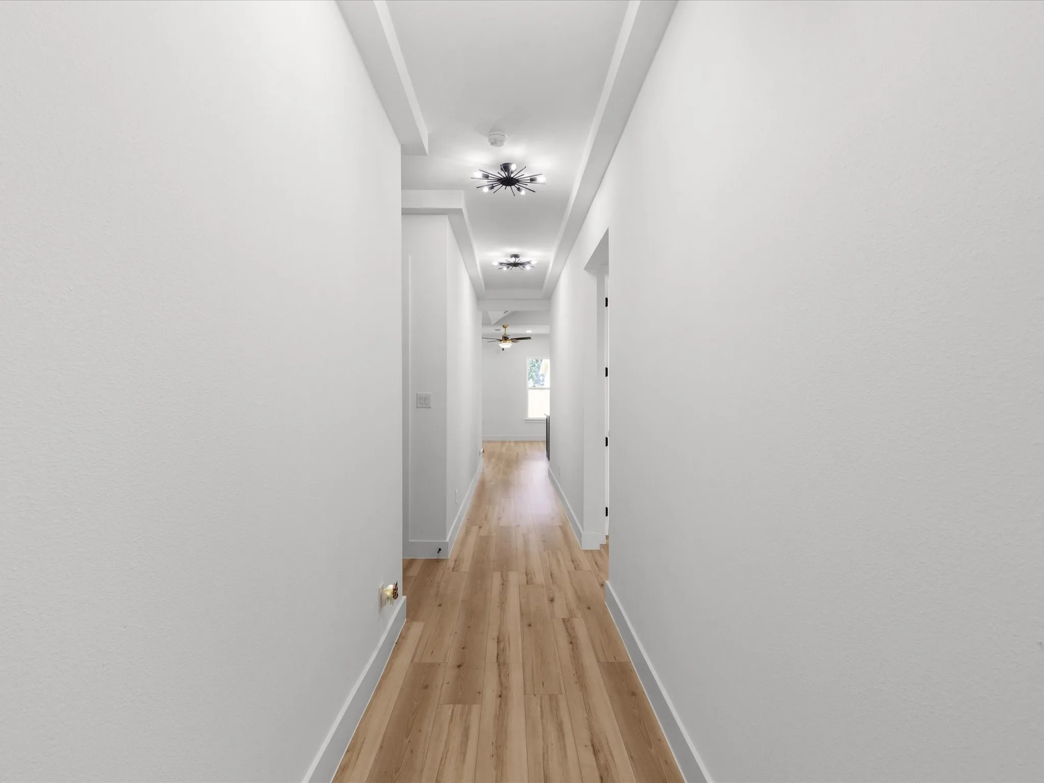 Hallway featuring light wood-finish flooring, white walls, and a tray ceiling