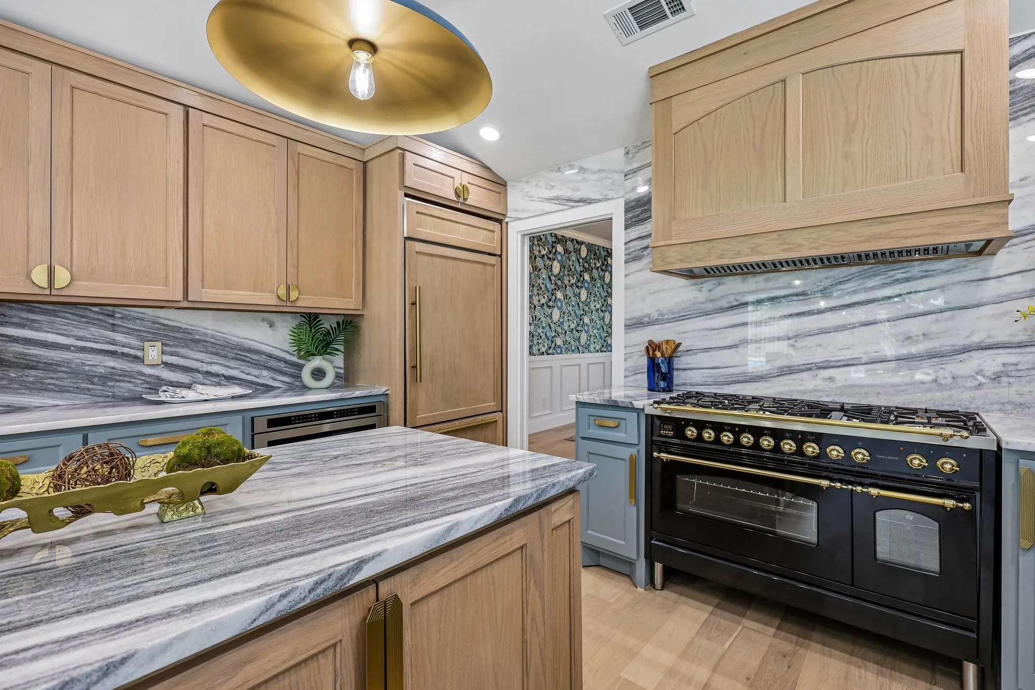 Gourmet kitchen featuring a built-in refrigerator, professional-grade range, custom light wood cabinetry, natural stone countertops, and a full-height stone backsplash