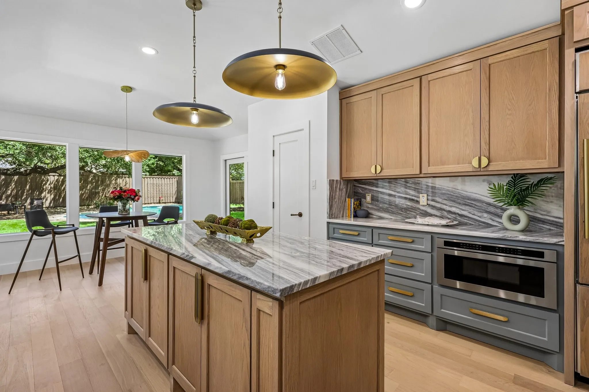 Kitchen featuring a large central island with a stone countertop, custom cabinetry in natural wood-tone and gray finishes, a built-in microwave, and wood-finish flooring