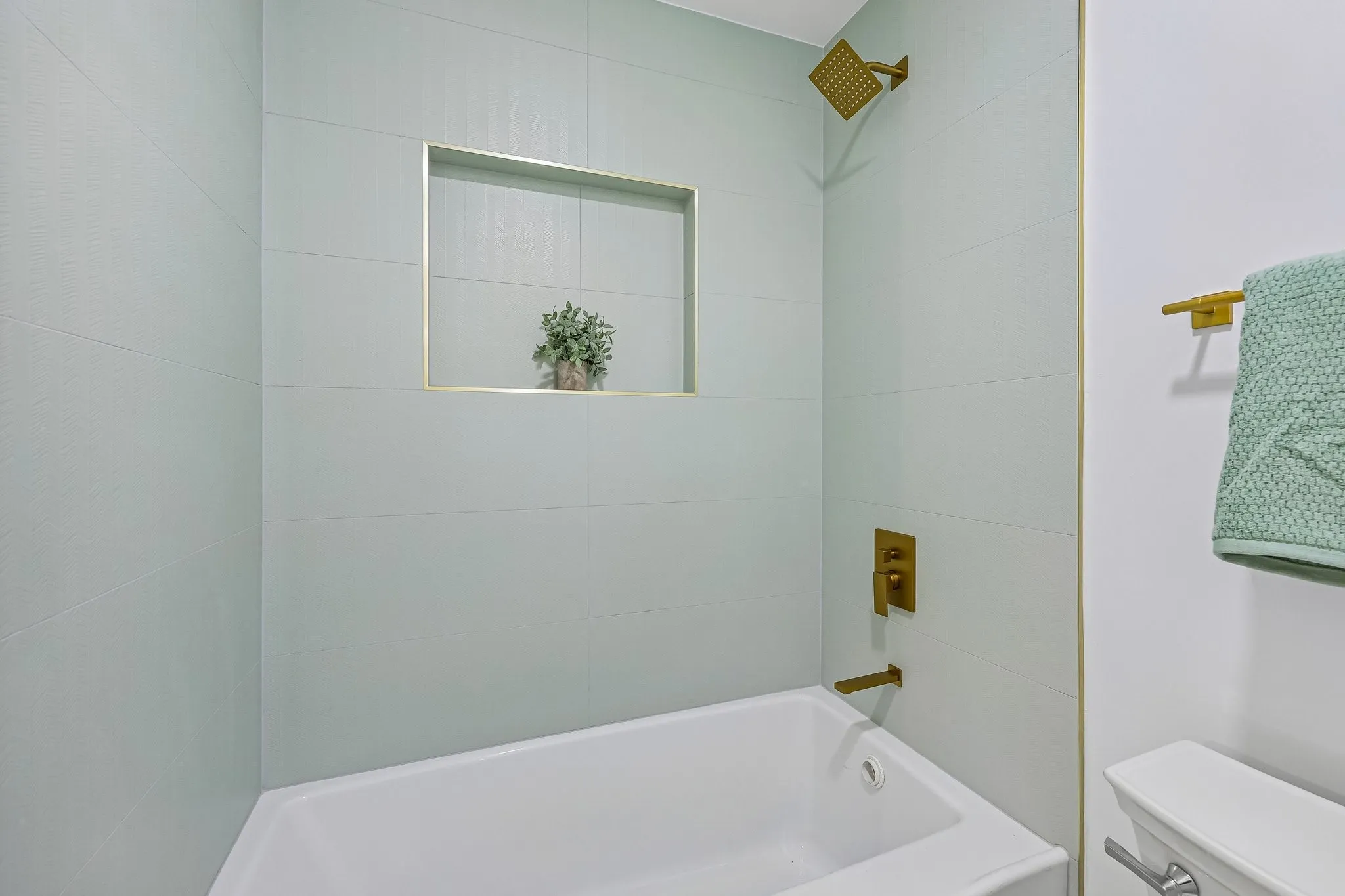Bathtub with light green tiled surround and contrasting brass fixtures