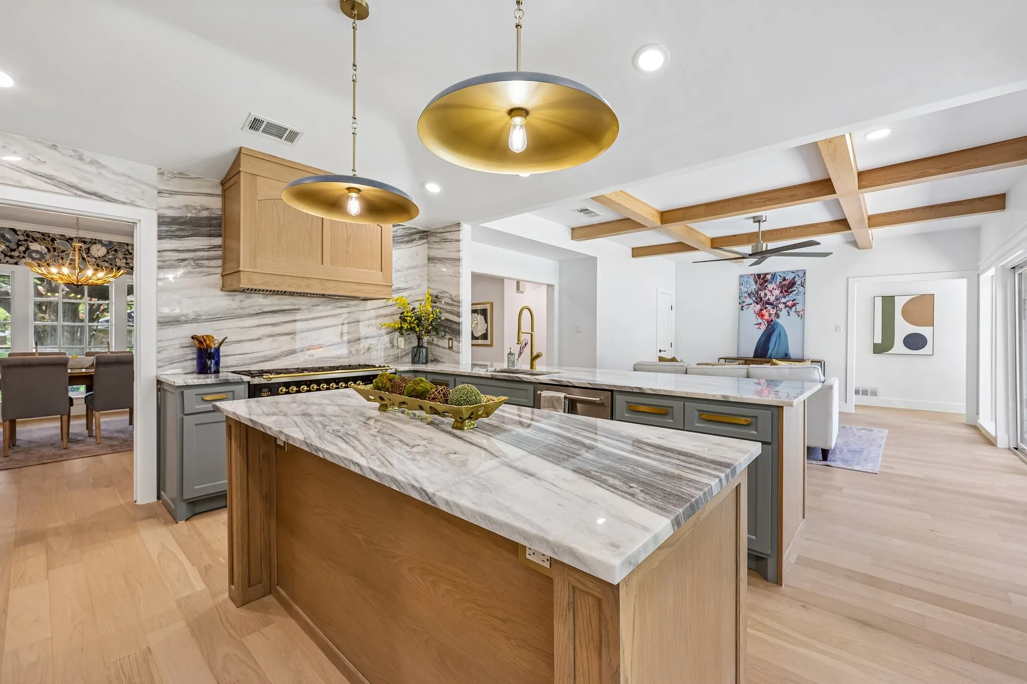 Gourmet kitchen featuring a large island with a natural stone countertop, wood-finish flooring, custom range hood, and brass pendant lighting