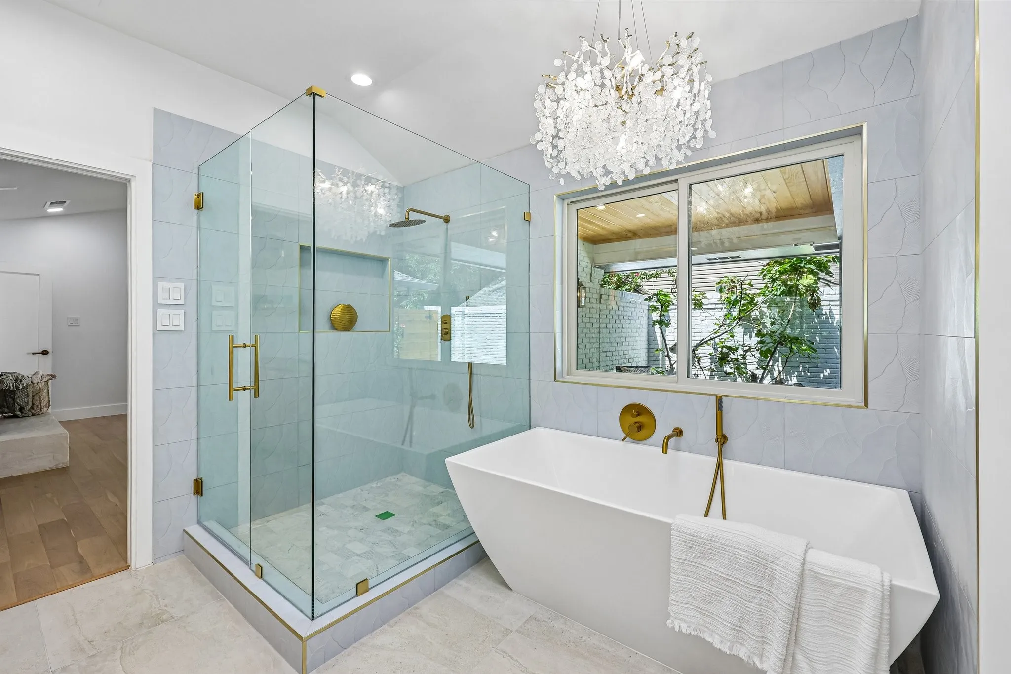 Spacious bathroom featuring a frameless glass shower enclosure with brass hardware, an integrated shower niche, and a contrasting hexagon tile shower floor