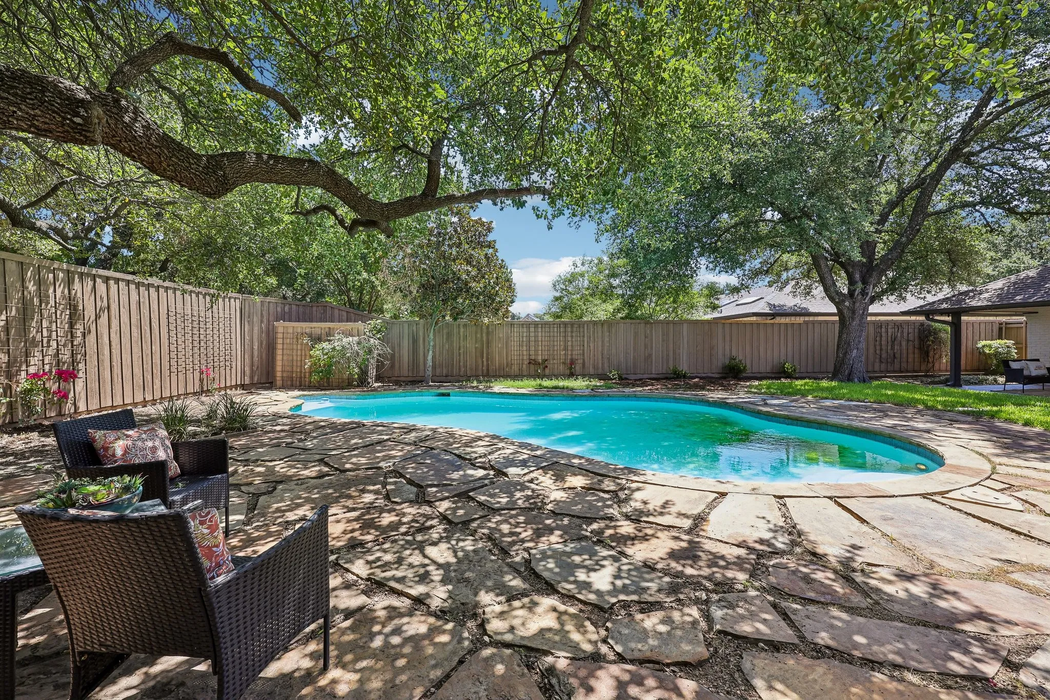 Expansive backyard featuring a freeform swimming pool, flagstone patio, mature trees providing natural shade, and a privacy fence