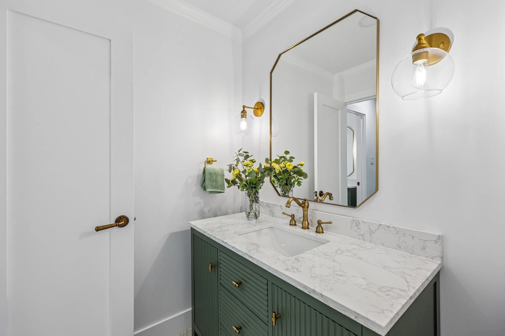 Powder room featuring a fluted green vanity with brass hardware, a white countertop, an undermount sink, and a gold-framed octagonal mirror