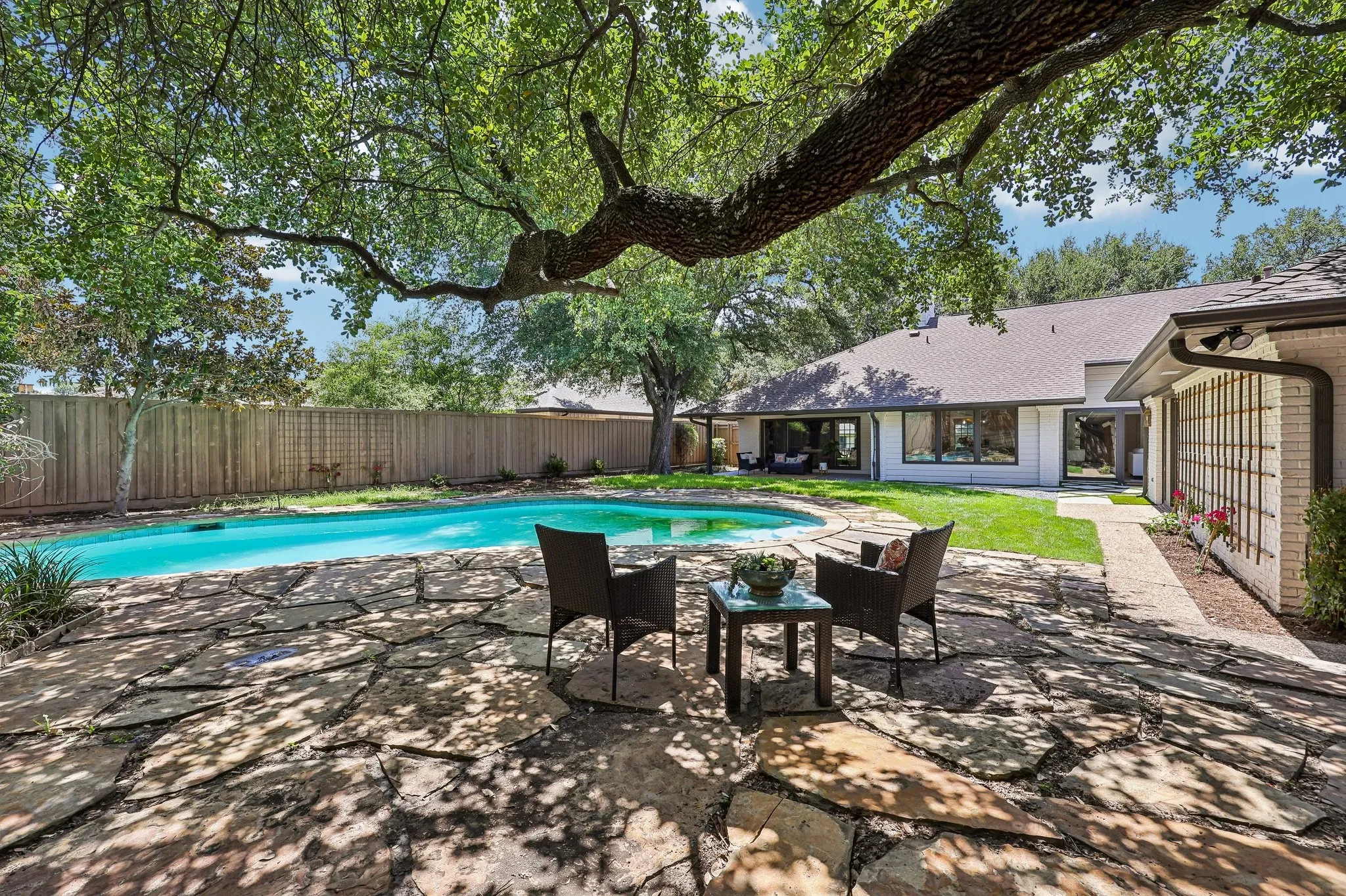 Expansive flagstone patio with an inground swimming pool, mature tree canopy, manicured lawn, and privacy fencing