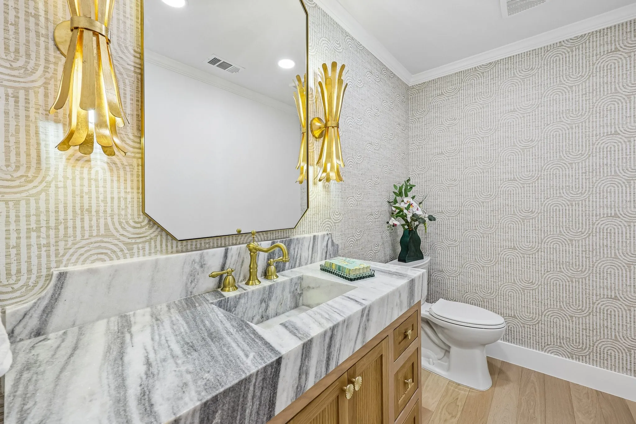 Powder room featuring a custom marble vanity with integrated sink, brass fixtures, a frameless octagonal mirror, and textured wallpaper