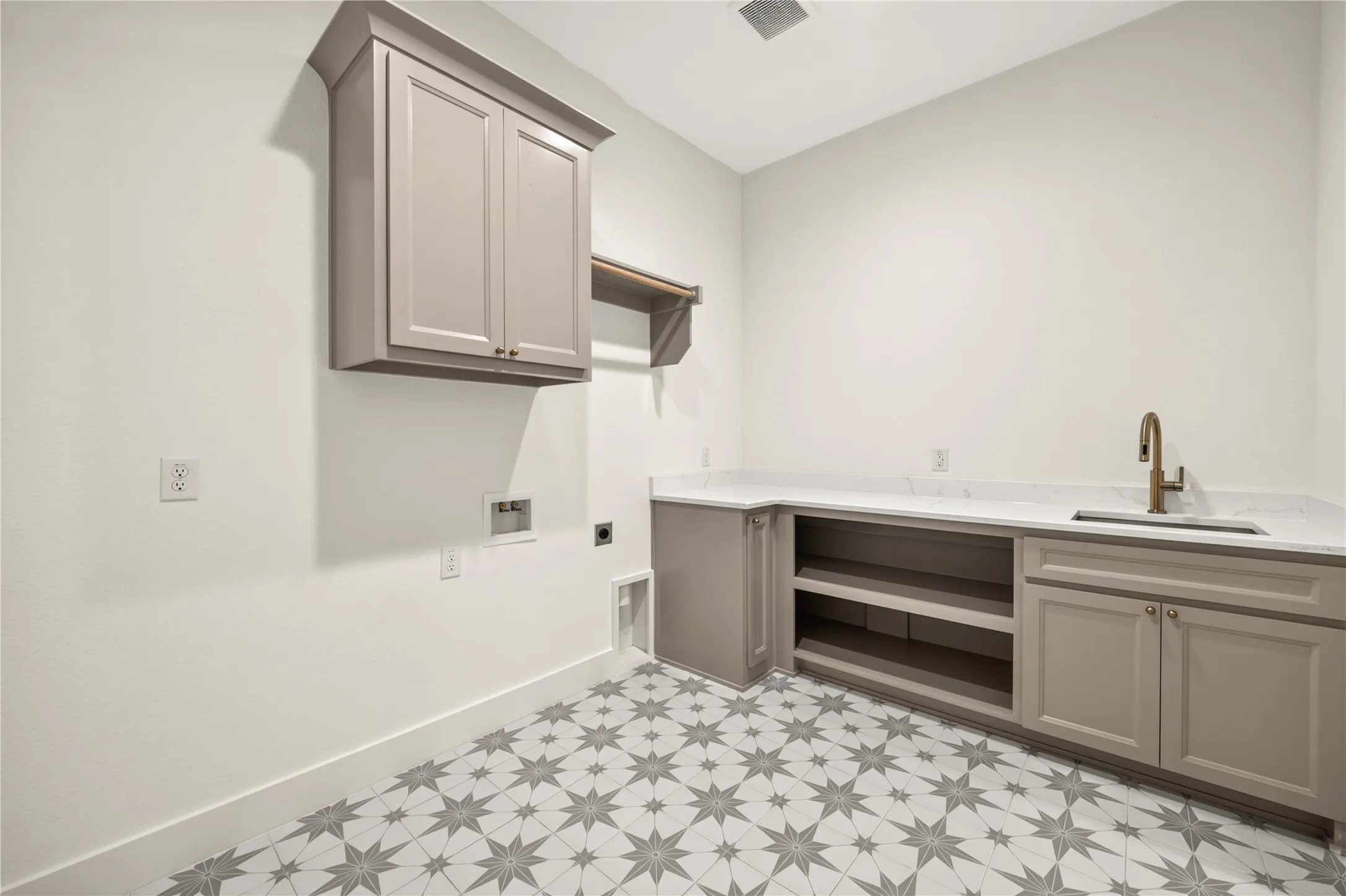 Utility room featuring patterned tile flooring, built-in cabinetry, a countertop with an integrated sink, and an elevated shelf