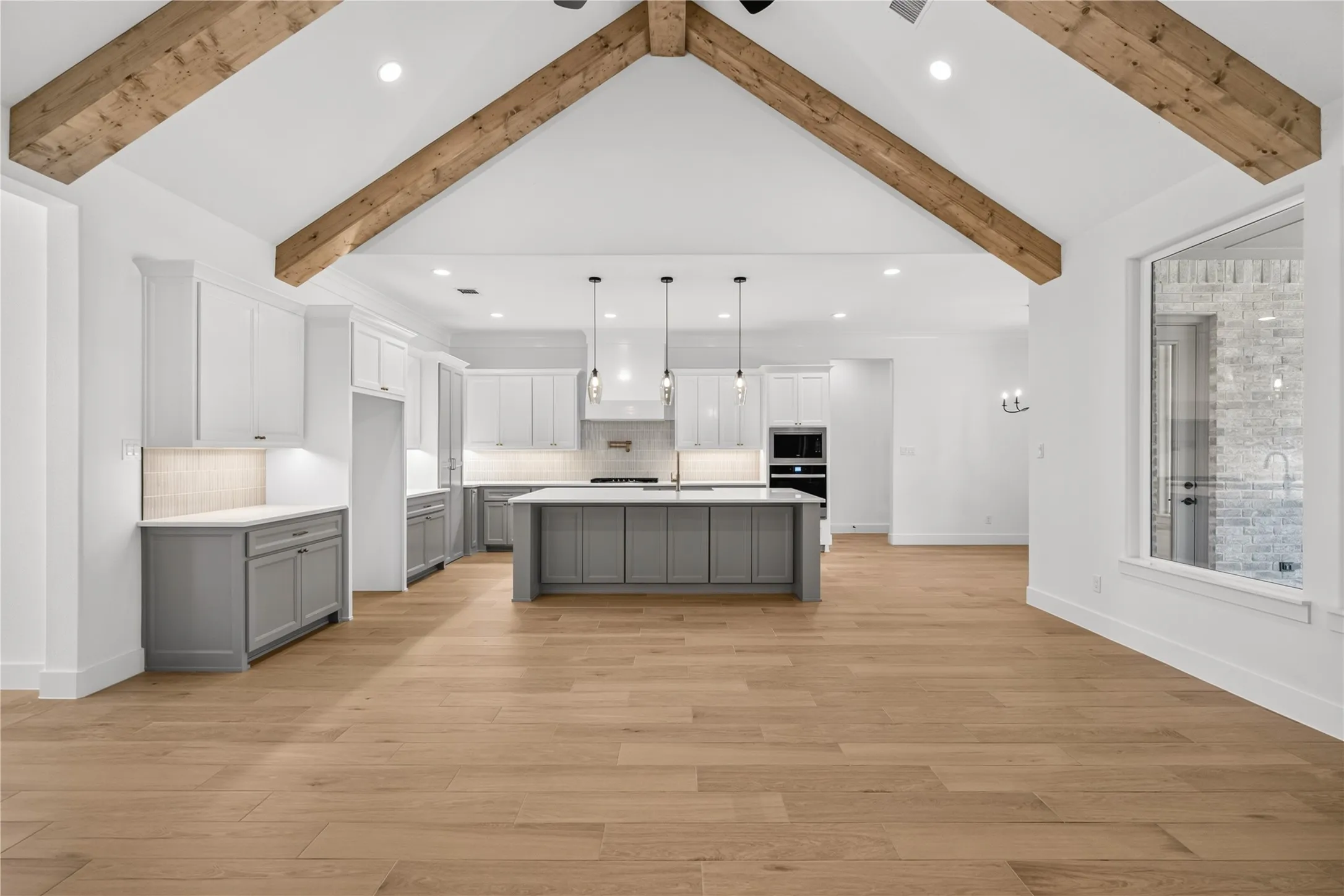Open-concept living space featuring wood-finish flooring, a vaulted ceiling with exposed wood beams, and a kitchen with two-toned cabinetry and a central island