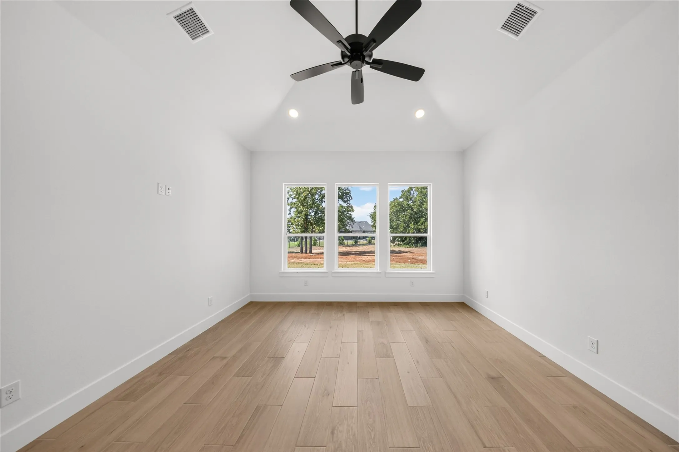 Spacious room featuring wood-finish flooring, a vaulted ceiling, and a modern ceiling fan