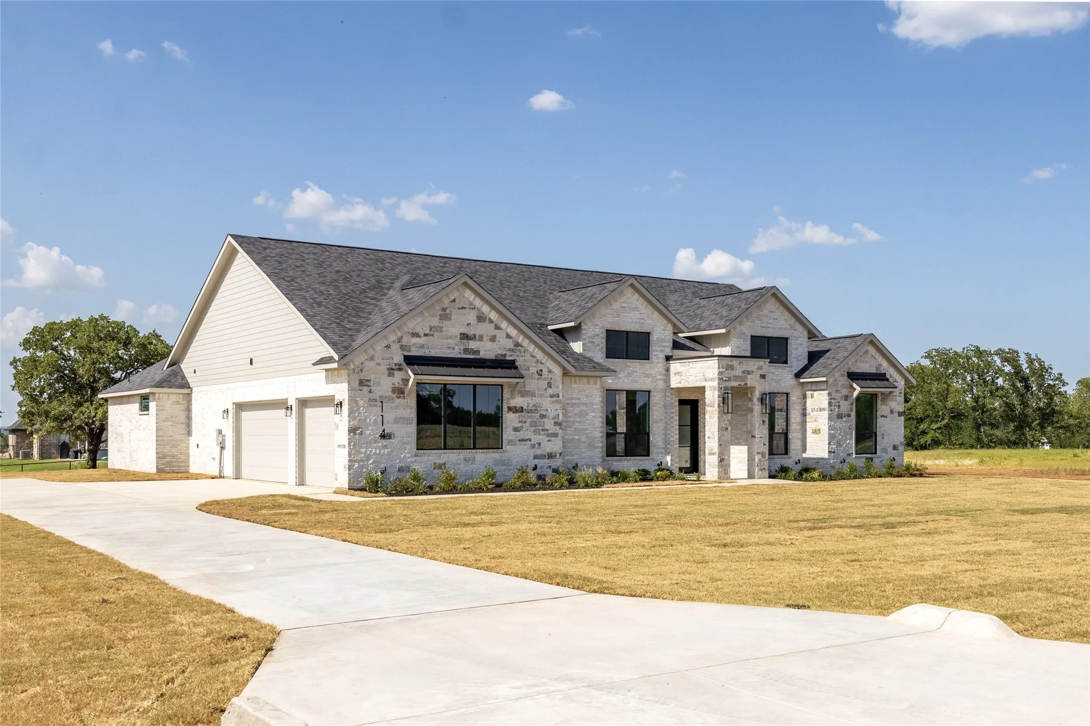 Contemporary stone and siding exterior featuring a multi-gable roofline, black-framed windows, an attached two-car garage, and a concrete driveway