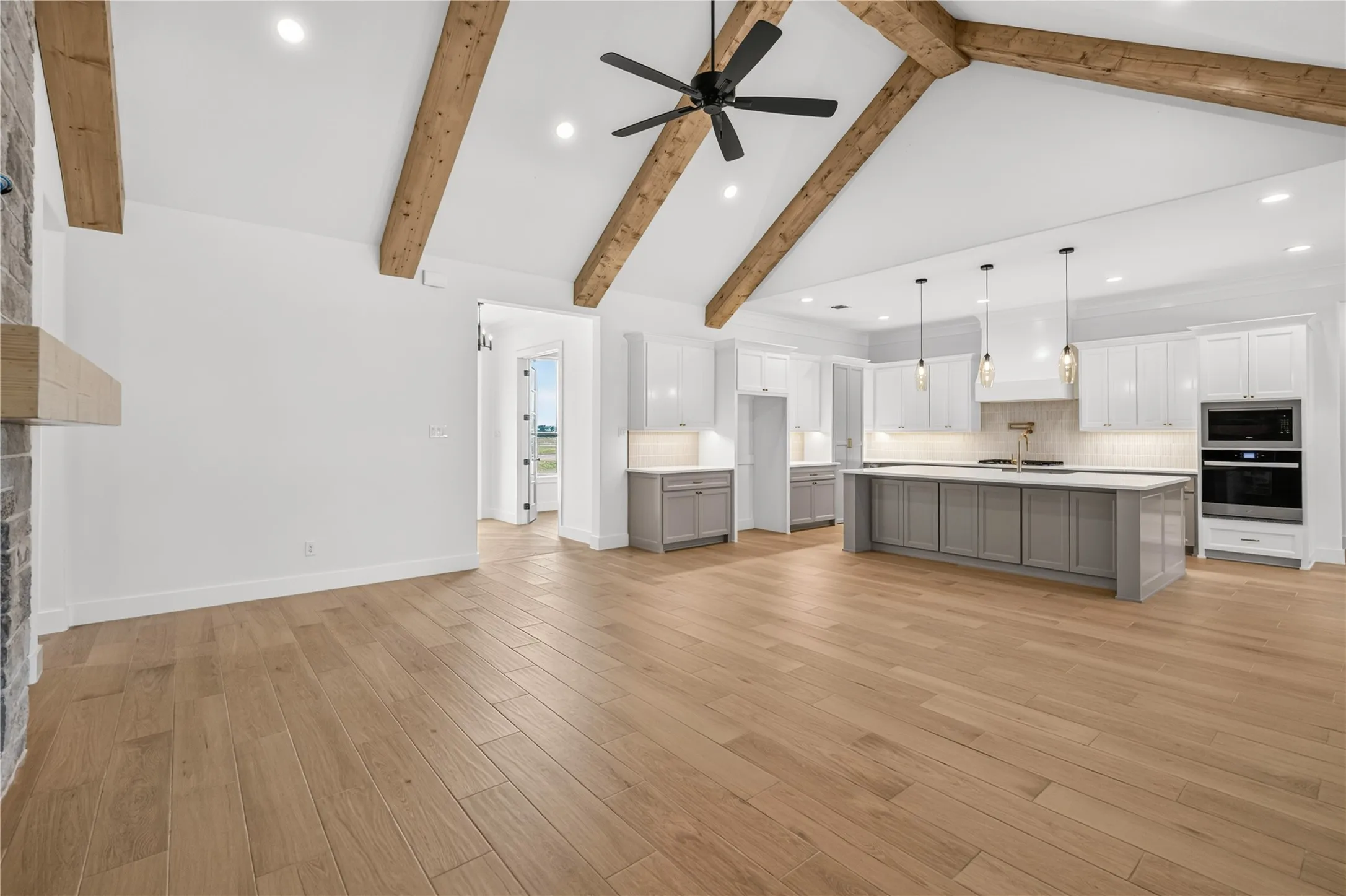 Expansive open-concept living area featuring a vaulted ceiling with exposed wood beams, wood-finish flooring, a modern kitchen island with pendant lighting, and built-in stainless steel appliances