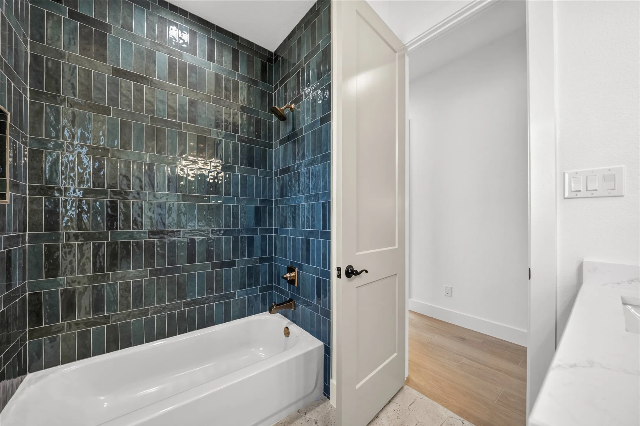 Bathtub and shower combination featuring dark blue and black subway tile surround, integrated shower niche, and bronze fixtures