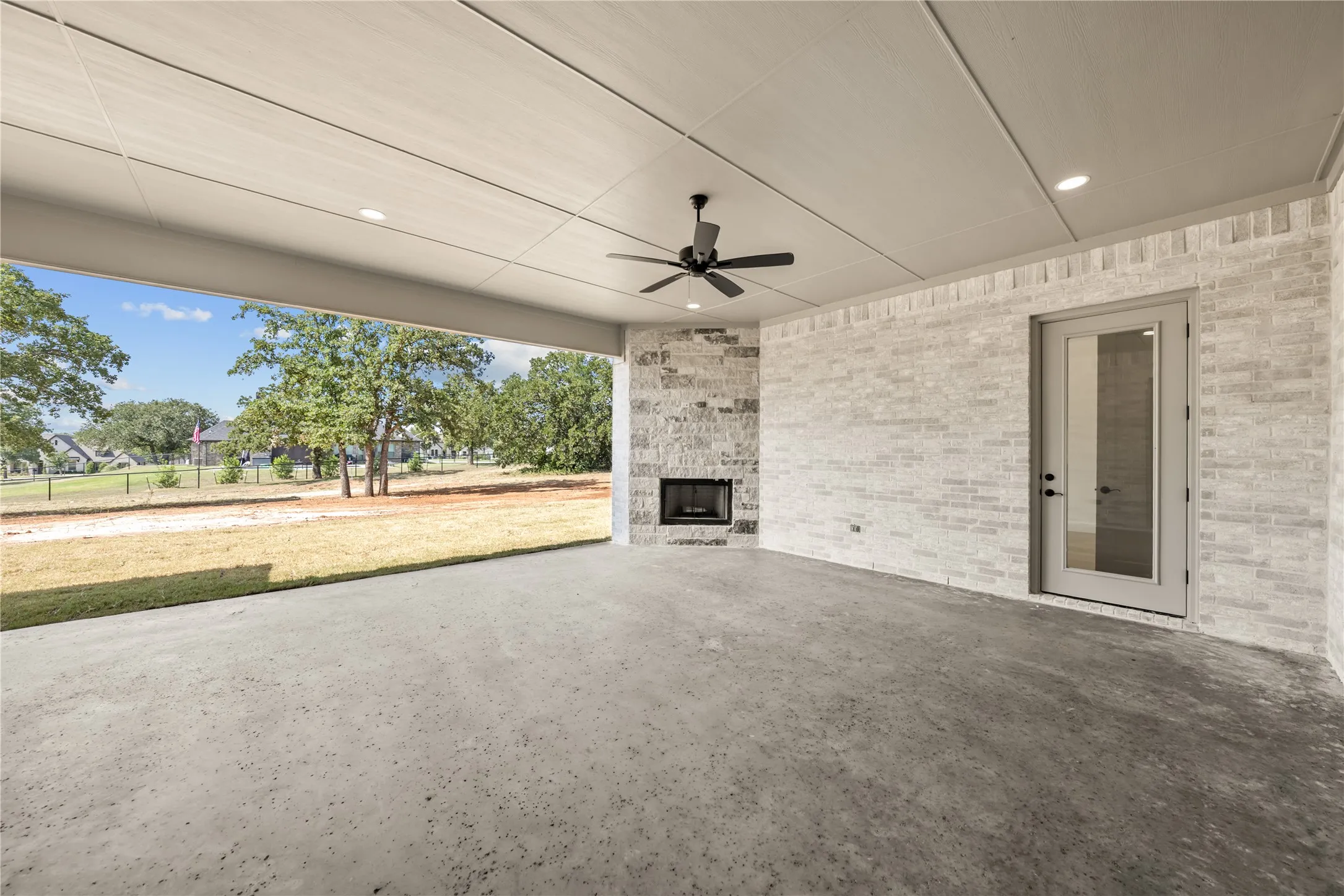 Covered outdoor patio featuring a concrete floor, light brick exterior, and a stone-clad fireplace