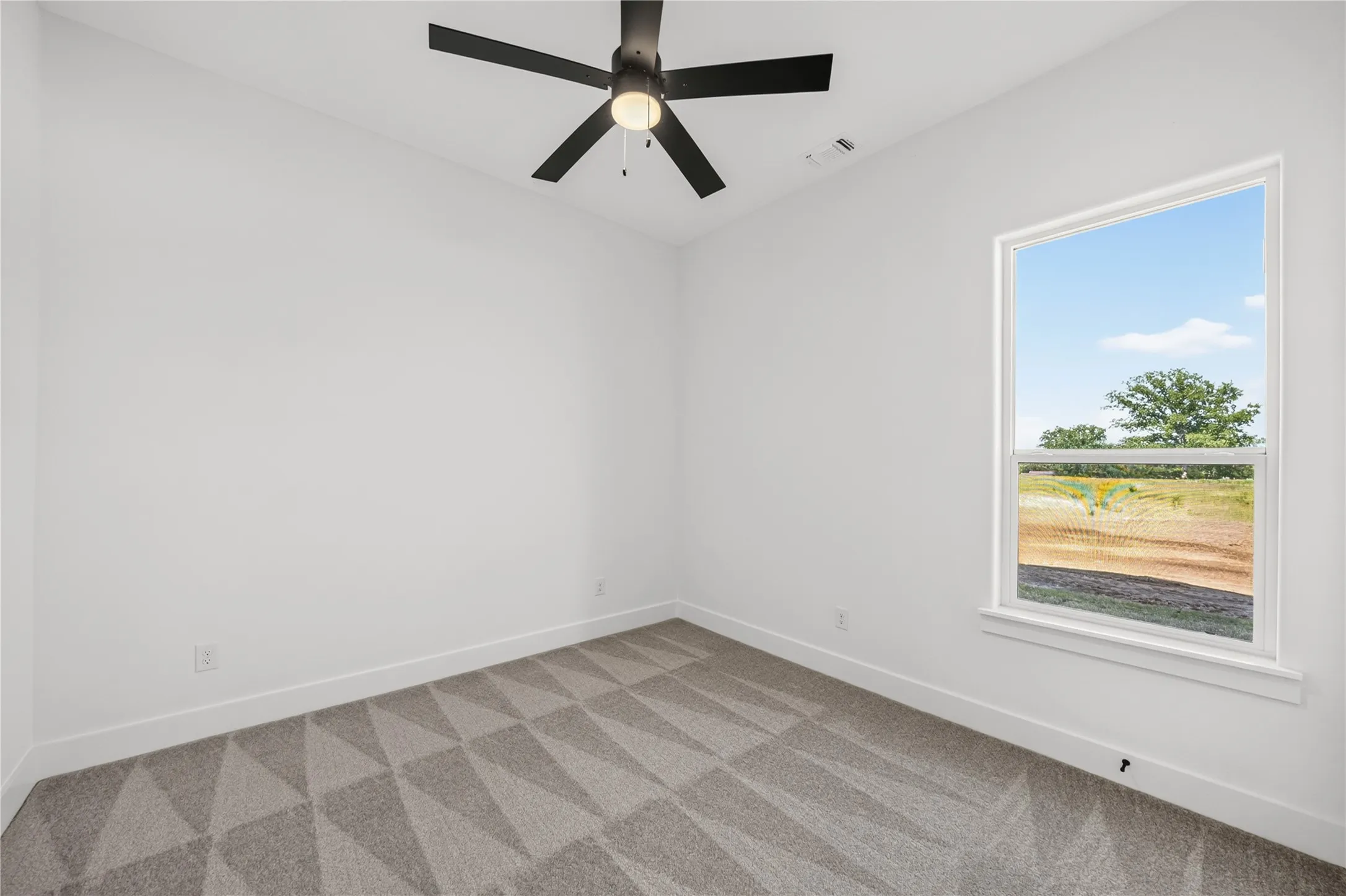 Bright room featuring a large window, neutral white walls, geometric pattern carpet, and a ceiling fan