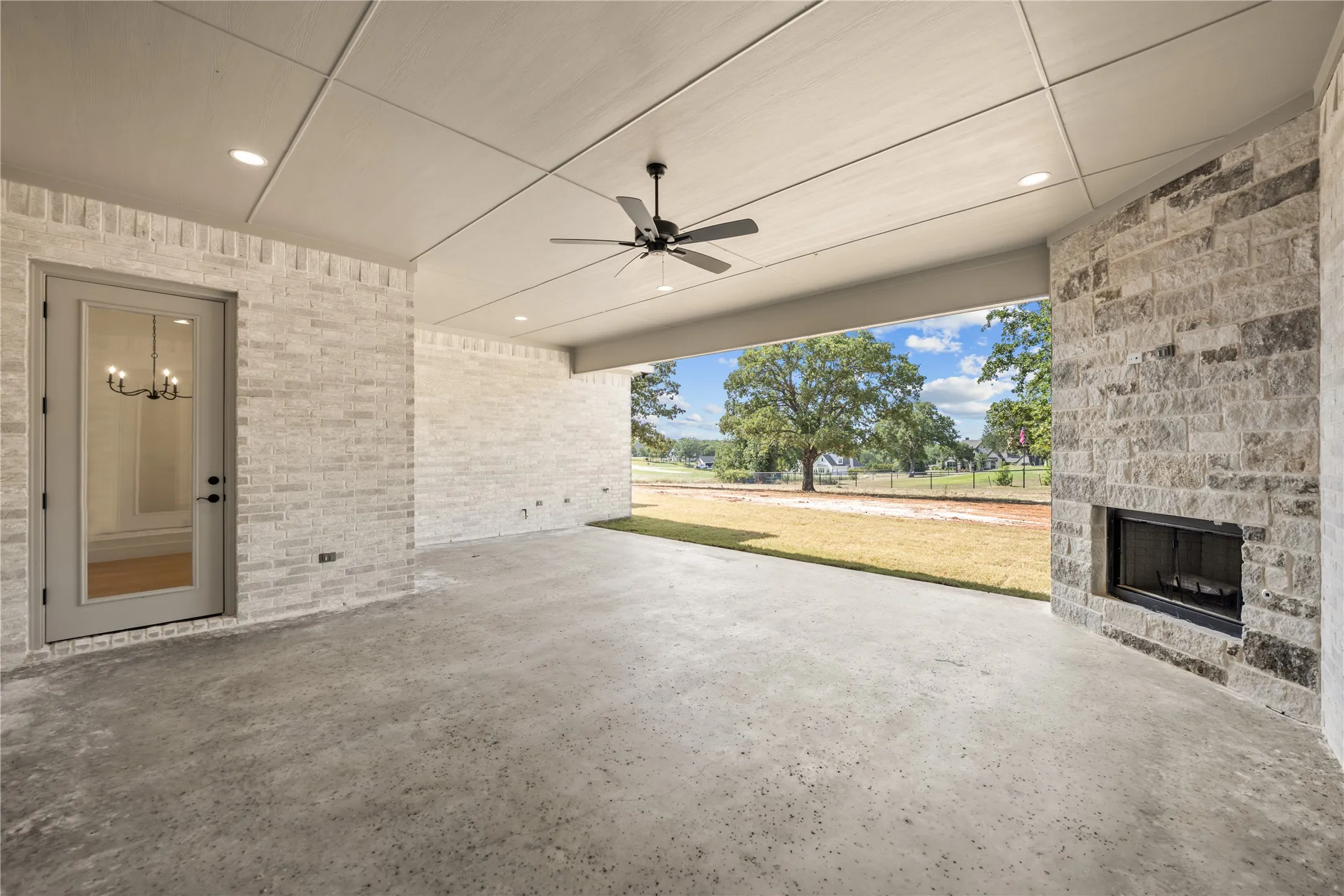 Expansive covered patio featuring a stone-clad fireplace and concrete flooring