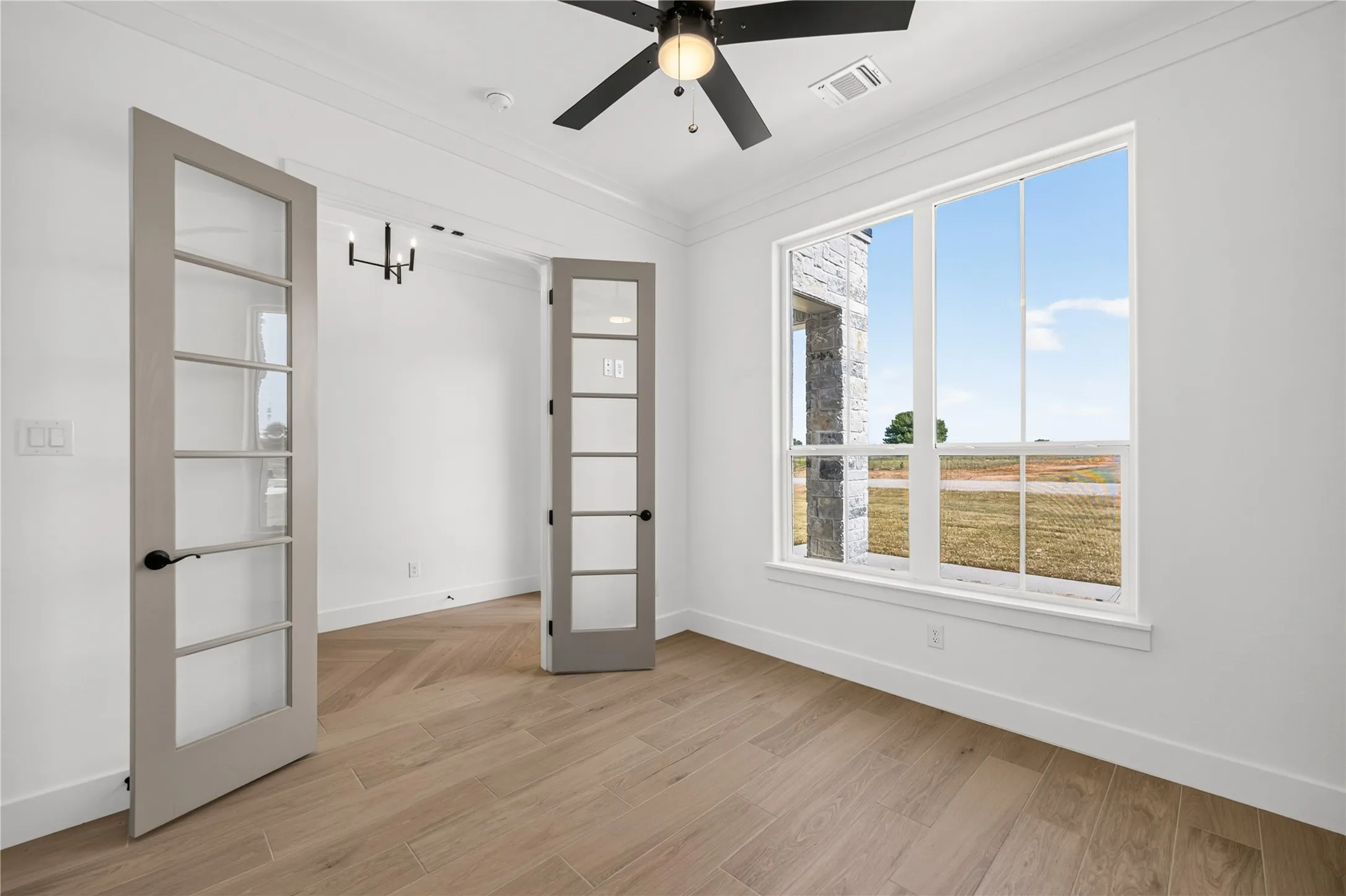 Room featuring wood-finish flooring in a herringbone pattern, a large multi-pane window, and two glass-paneled French doors
