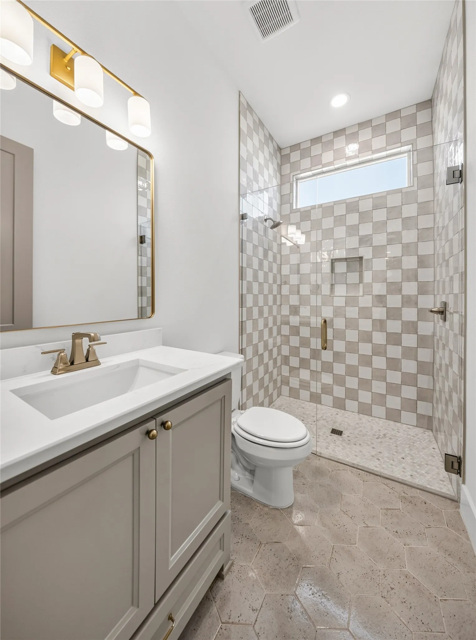 Bathroom featuring a walk-in shower with checkerboard tiling, a white vanity with a rectangular sink, gold-finish fixtures, and hexagonal floor tiles