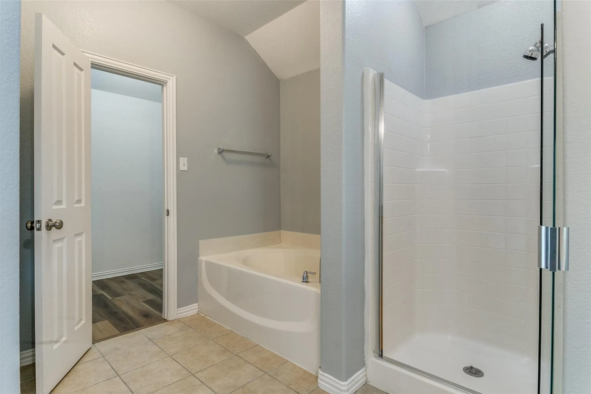 Bathroom featuring an enclosed shower, a corner soaking tub with deck-mounted fixtures, and light-toned tile flooring