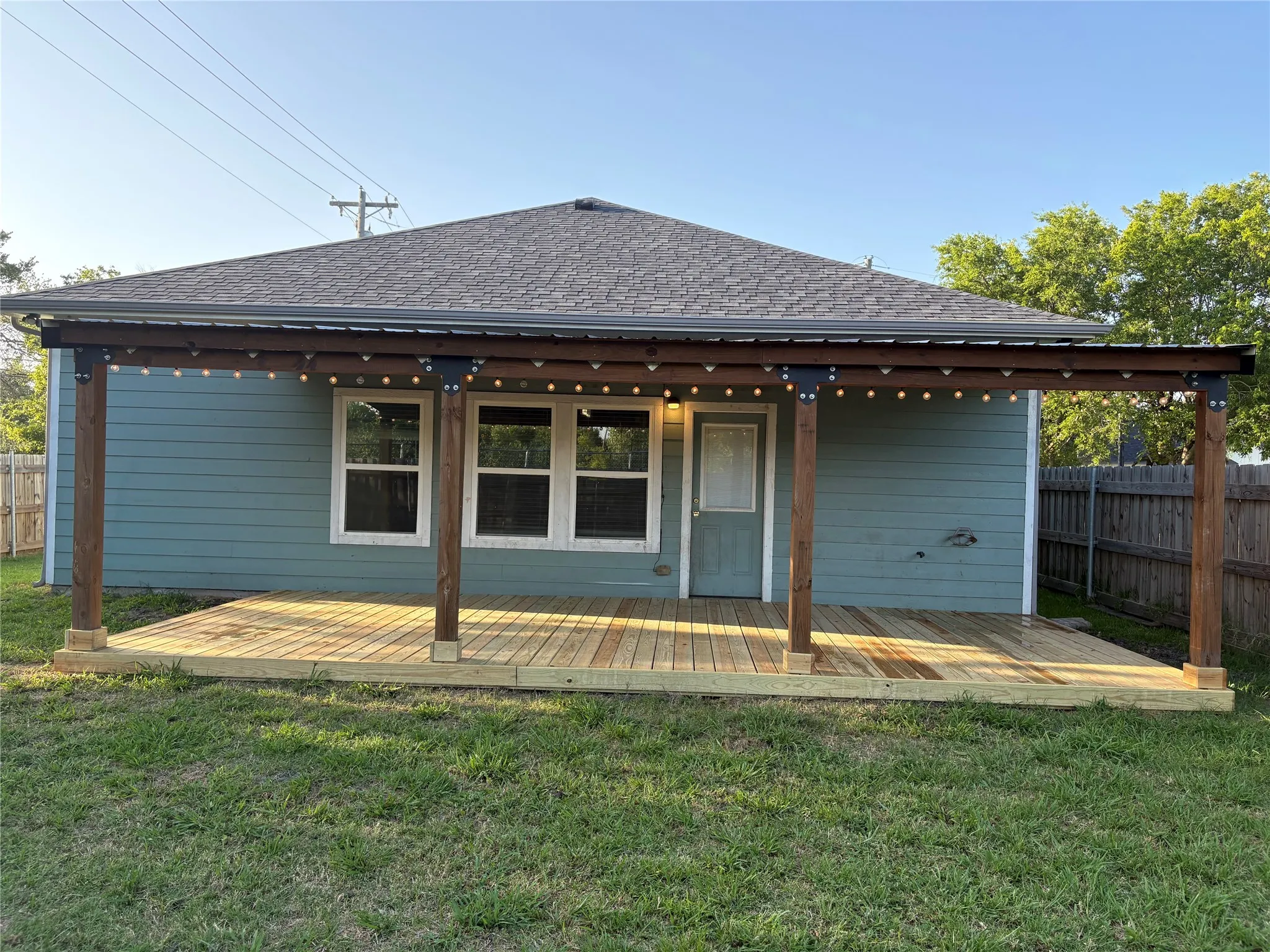 Expansive backyard featuring a new wood deck, a covered patio with string lighting, a light blue exterior, and a wood privacy fence