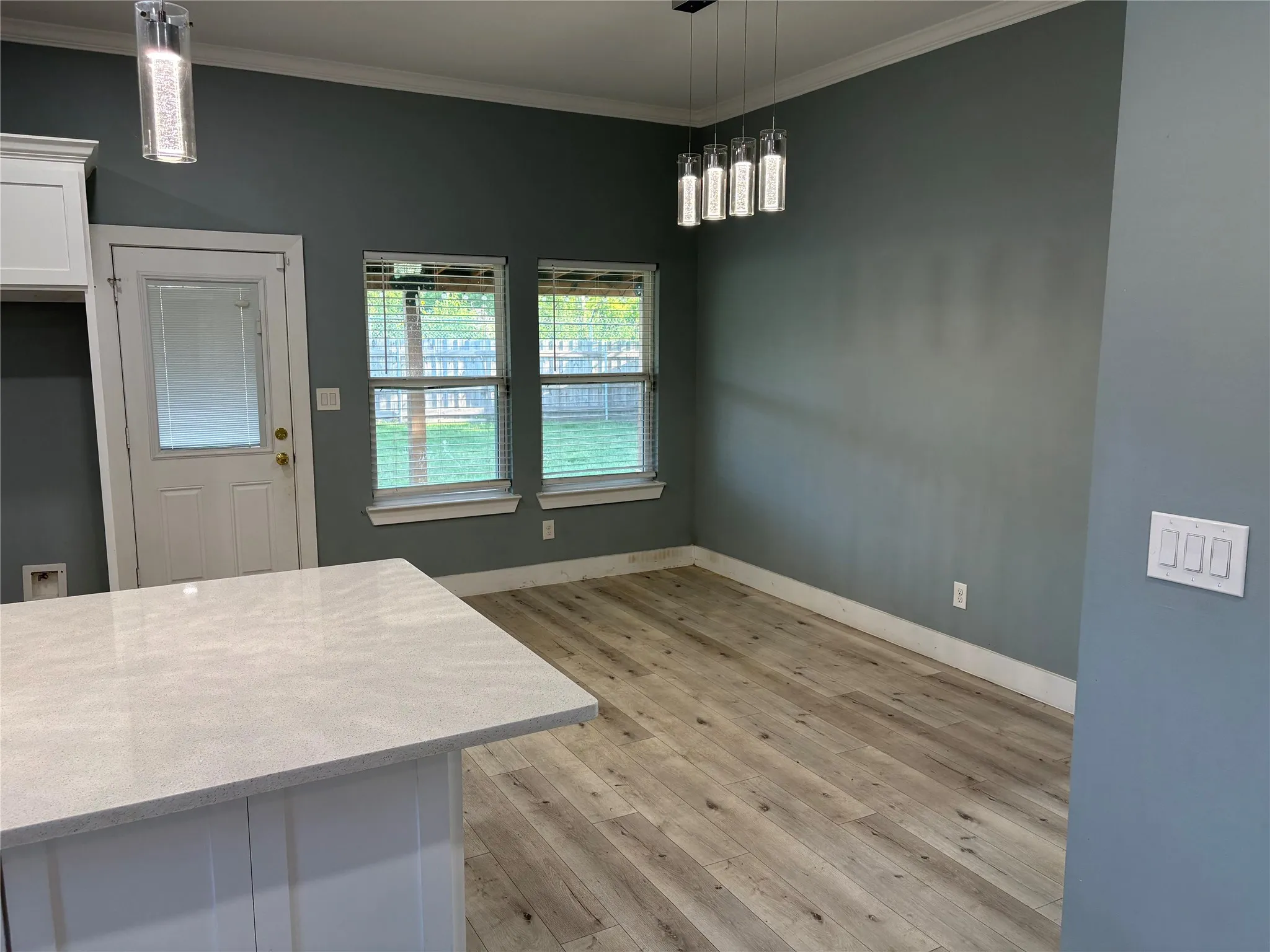 Open-concept living space featuring wood-finish flooring, a contemporary linear chandelier, and a white countertop island