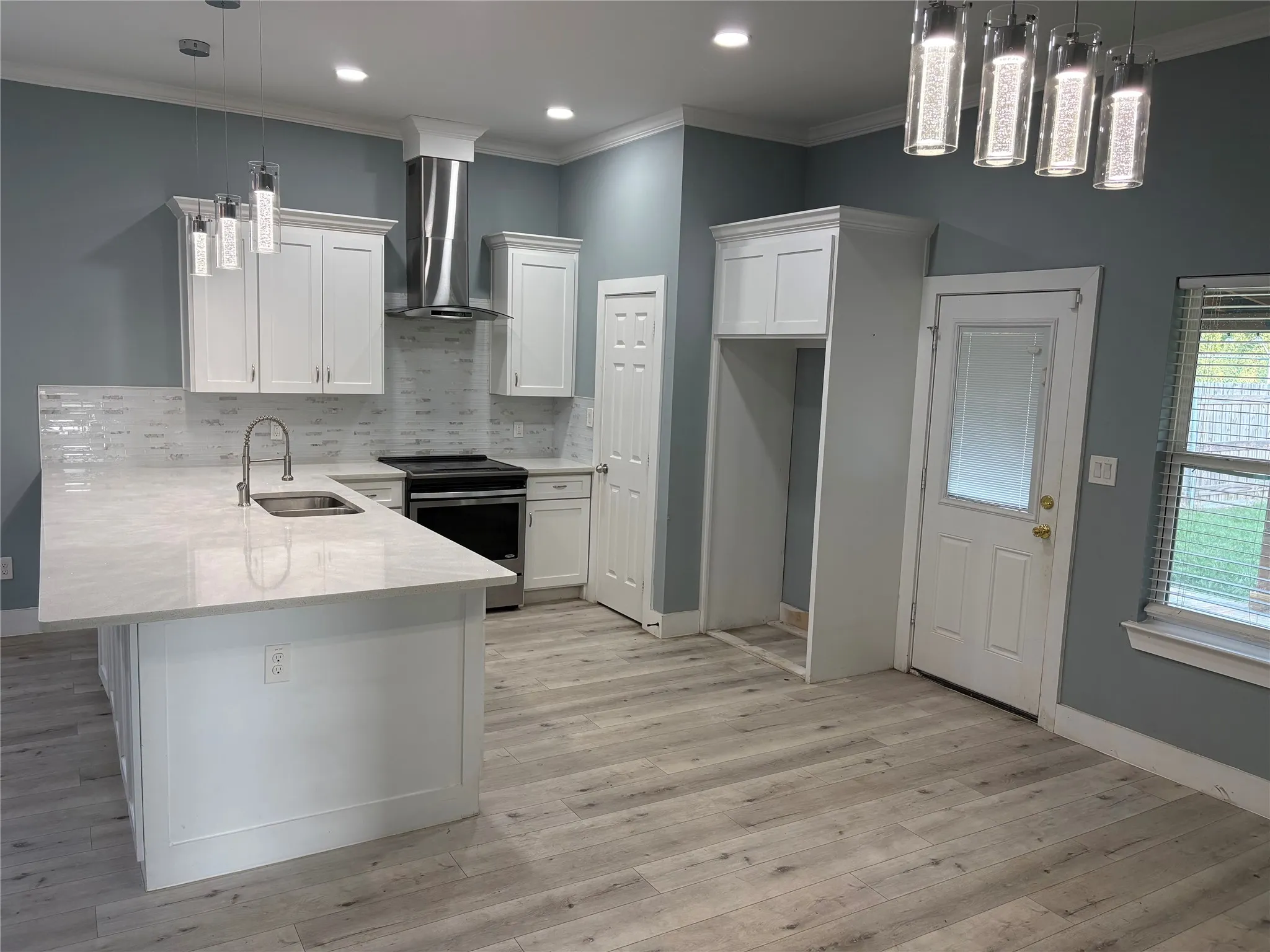Contemporary kitchen featuring white cabinetry, a large center island with a sink, white patterned backsplash, and light wood-finish flooring