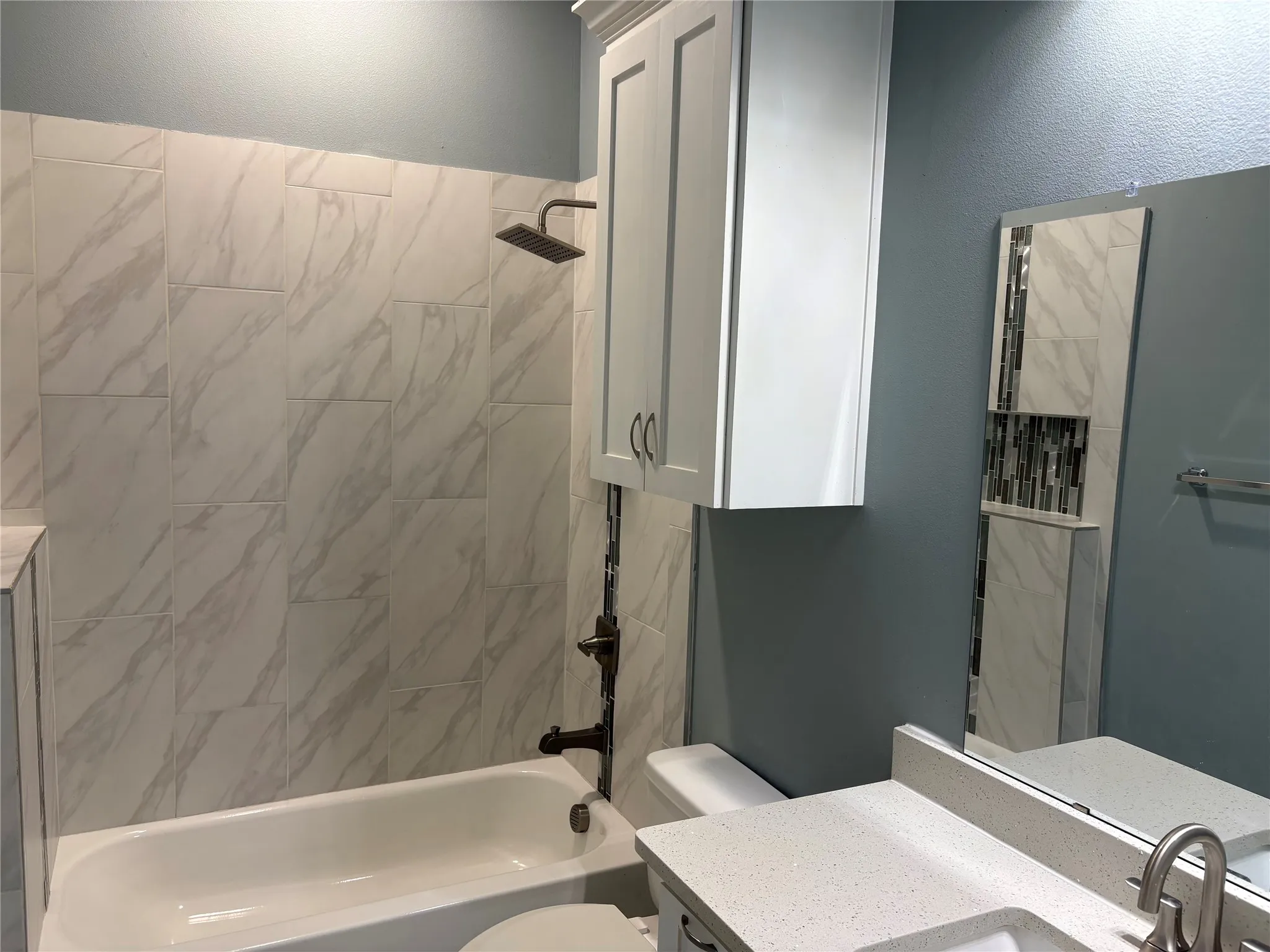 Bathroom featuring a white bathtub, white marble-look shower tile, and a rainfall showerhead