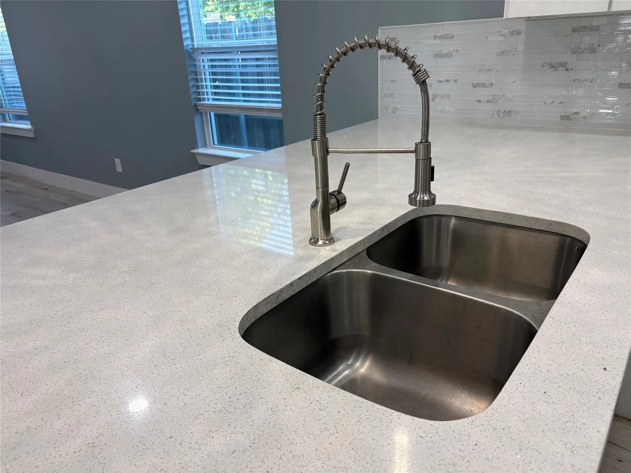White speckled countertop featuring an undermount double basin sink with a commercial-style faucet