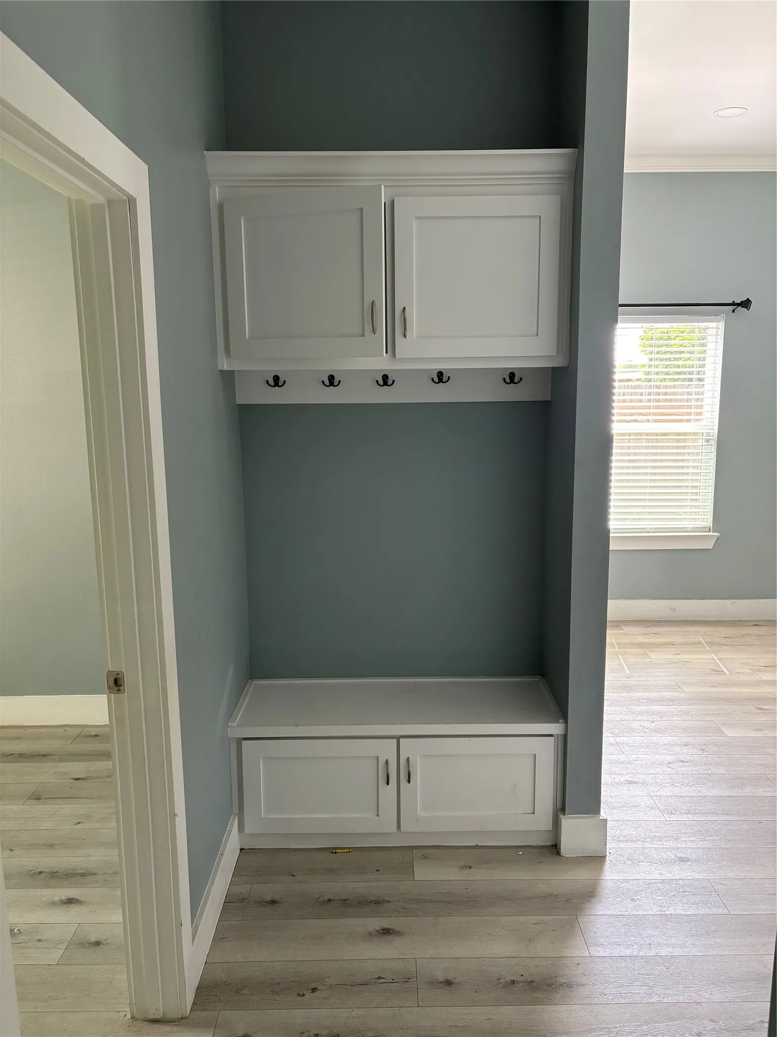 Integrated mudroom-style built-in featuring white shaker cabinetry, an upper storage unit with crown molding, a lower bench with cabinet storage, and a row of five dark-finish coat hooks