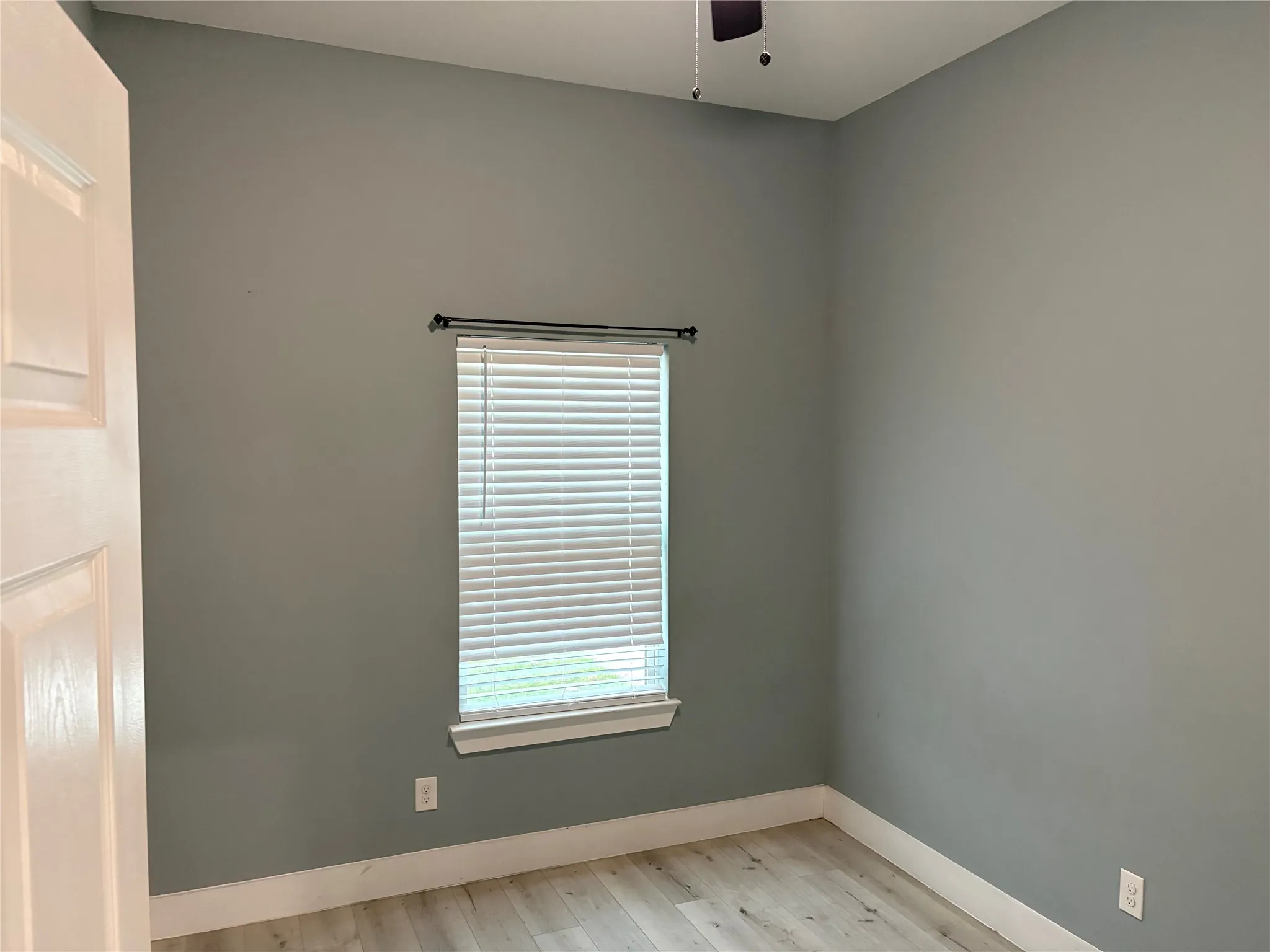 Interior room featuring light gray walls, wood-finish flooring, and white baseboards