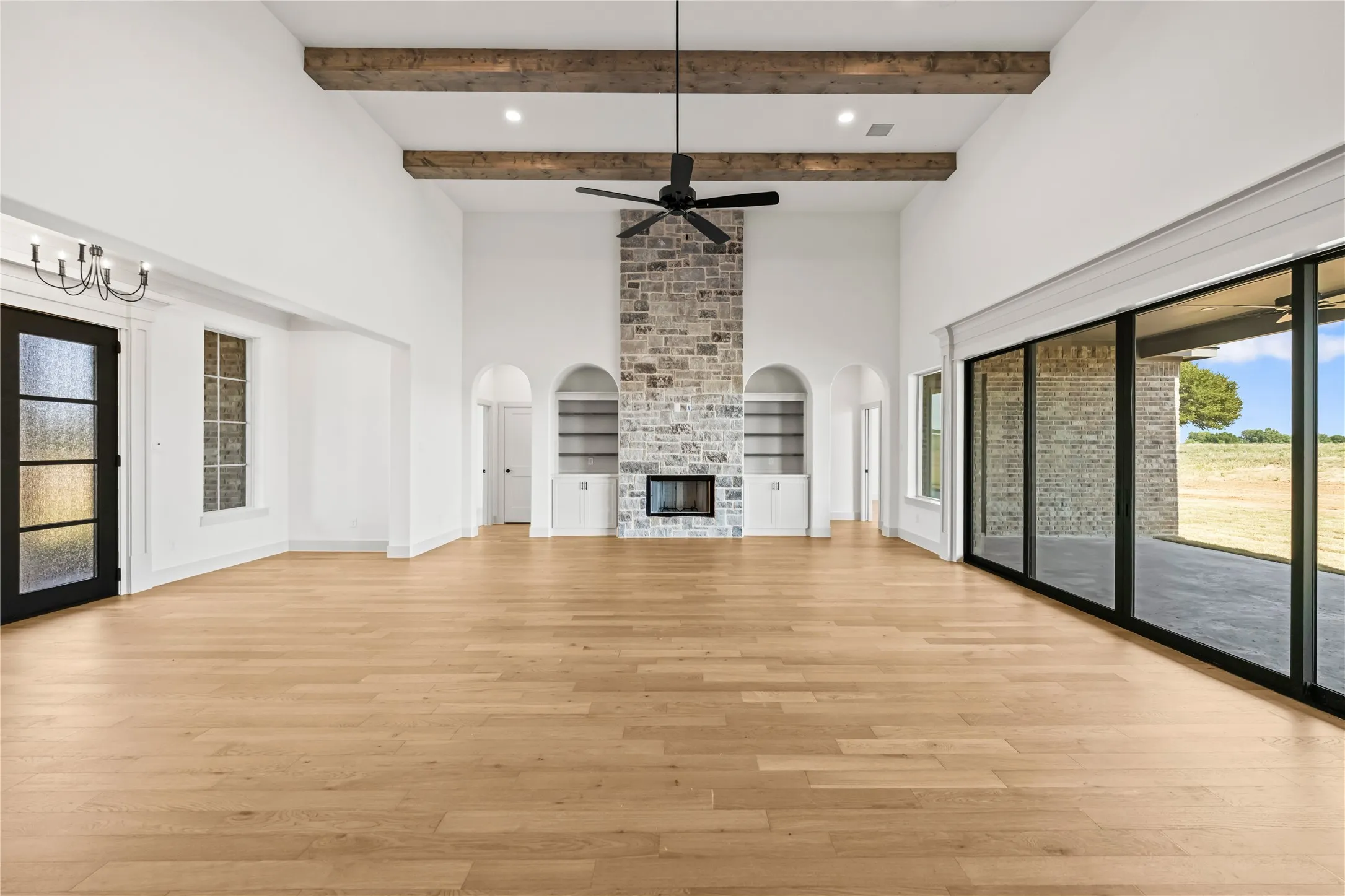 Spacious interior featuring a stone-clad fireplace with built-in shelving, soaring vaulted ceilings with exposed wood beams, and extensive wood-finish flooring