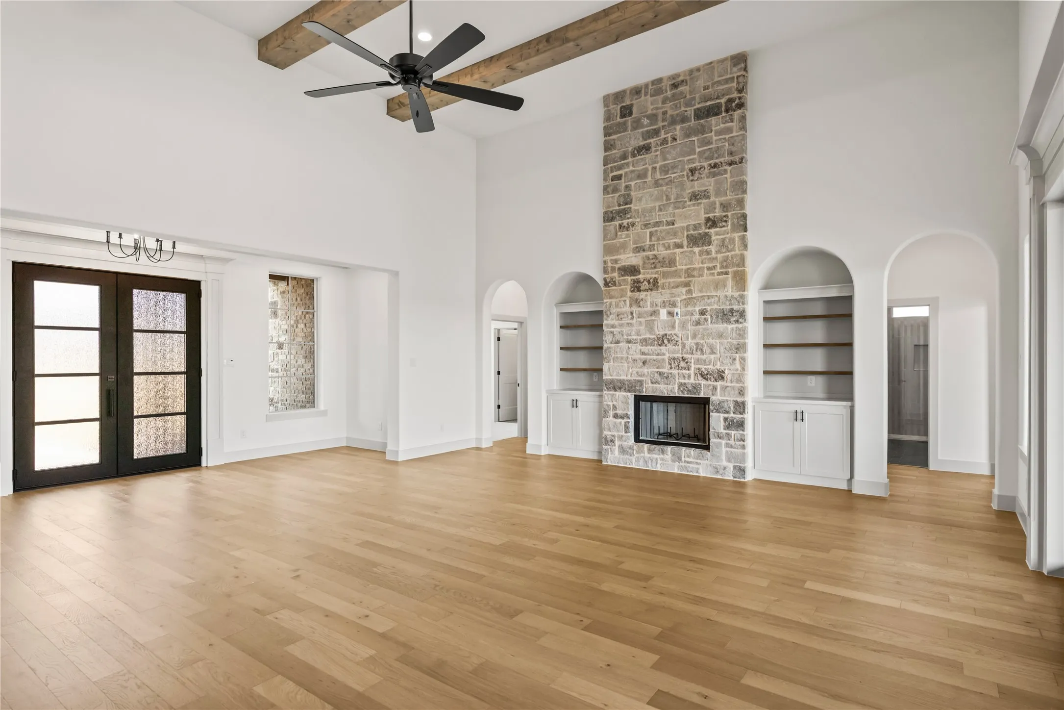 Spacious room featuring high vaulted ceilings with wood beams, a stone-clad fireplace, and wide plank wood-finish flooring