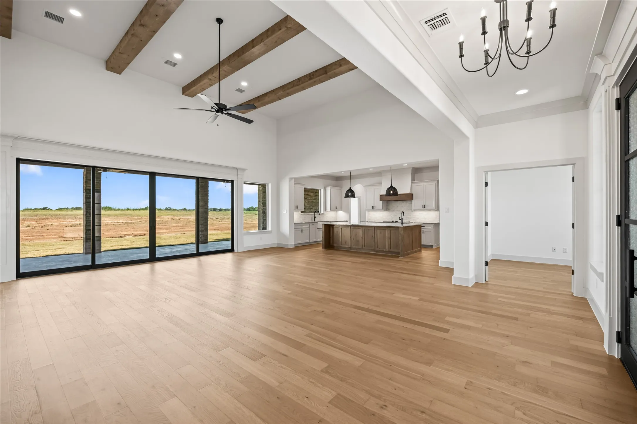 Spacious open-concept living area featuring light wood-finish flooring, high vaulted ceilings with exposed wood beams, and a large multi-panel sliding glass door