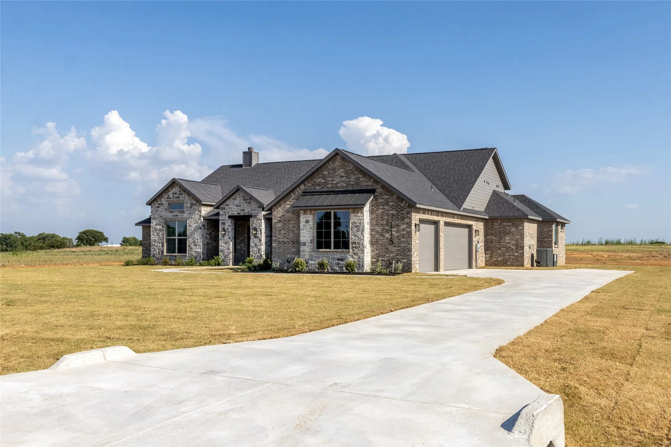 Traditional-style residence featuring a combination stone and brick exterior, dark shingle roof, and a two-car garage
